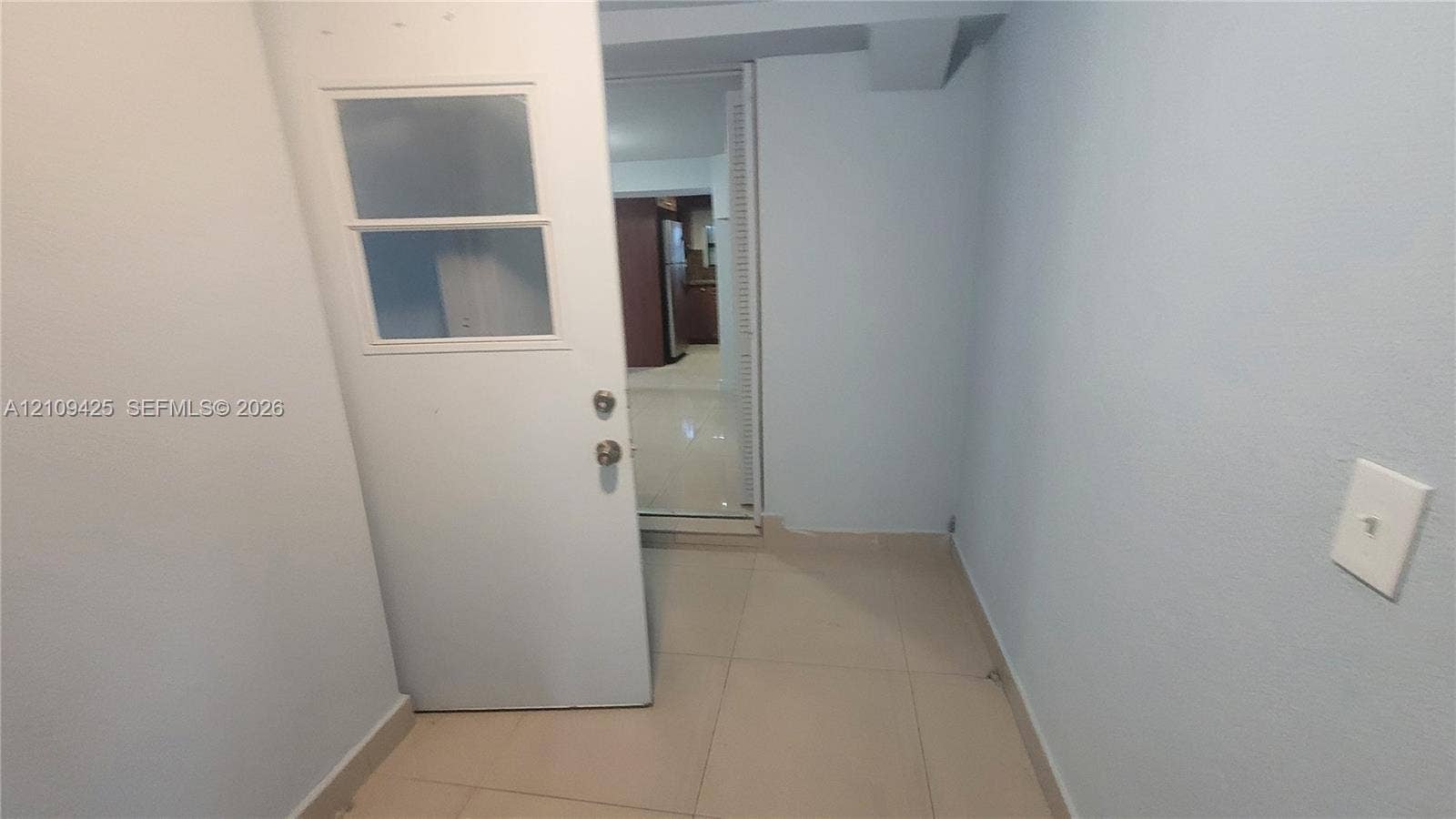 615 NW 25th Court, #B, Miami, Miami, FL 33125 Interior space featuring large-format ceramic tile flooring, a single-lite glass panel door with satin nickel hardware, and smooth-finish walls