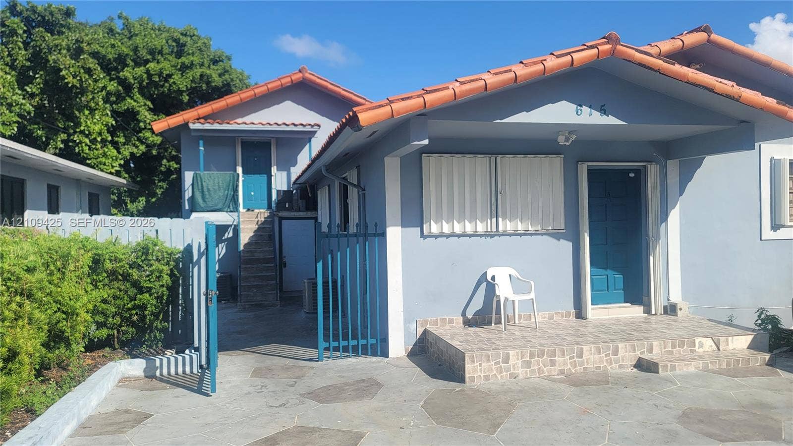 615 NW 25th Court, #B, Miami, Miami, FL 33125 Exterior facade featuring a tile roof, covered front porch with tiled flooring, stone-paved driveway, and metal security gate