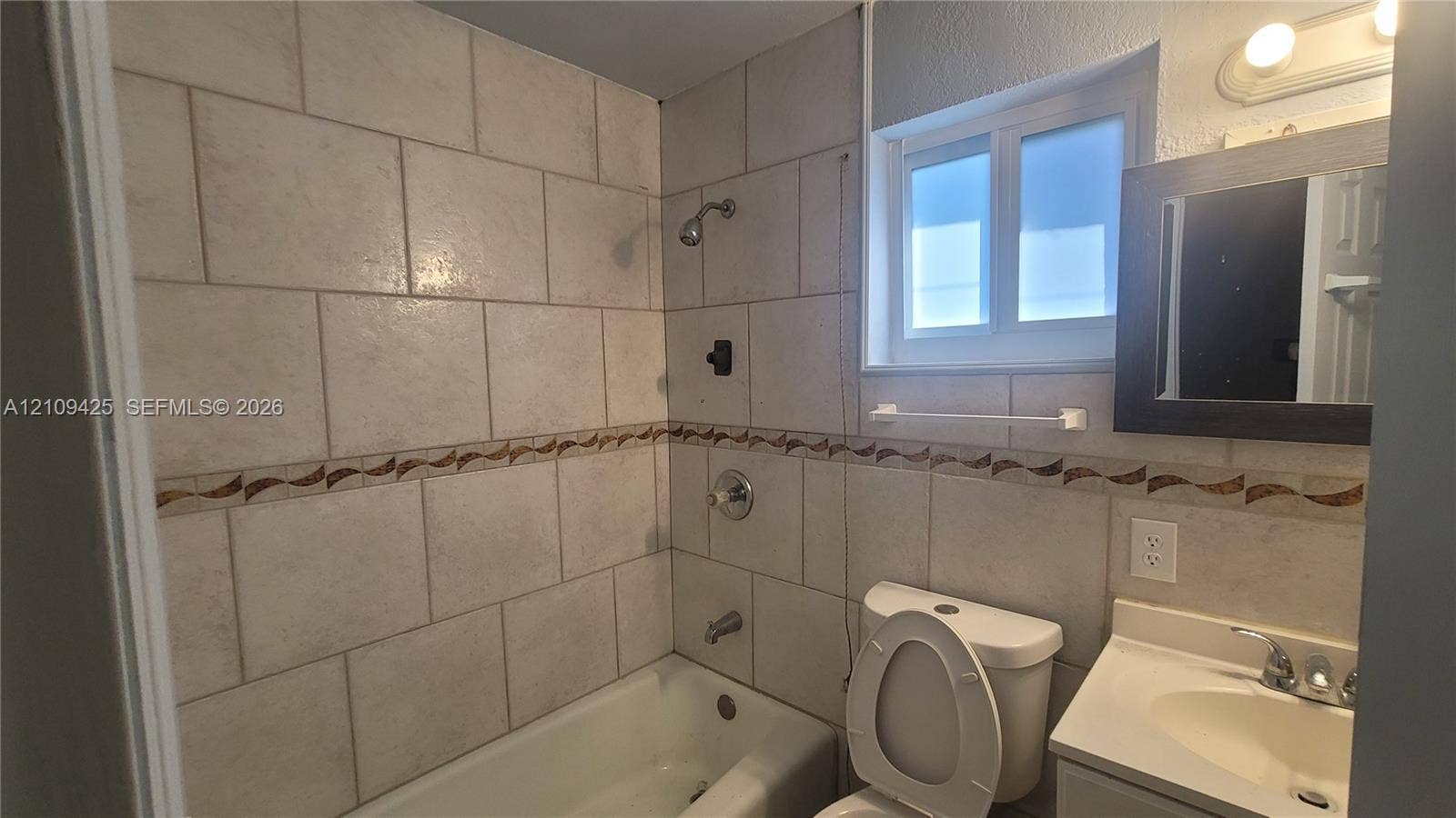 615 NW 25th Court, #B, Miami, Miami, FL 33125 Bathroom featuring a tub-shower combination, wall-mounted vanity with a single basin, inset mirror, and tiled walls with decorative mosaic accents