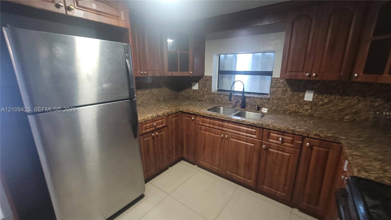 615 NW 25th Court, #B, Miami, Miami, FL 33125 Kitchen featuring stained wood cabinetry, stone-surface countertops, dual-basin stainless steel sink with high-arc faucet, stainless steel refrigerator, and ceramic tile flooring
