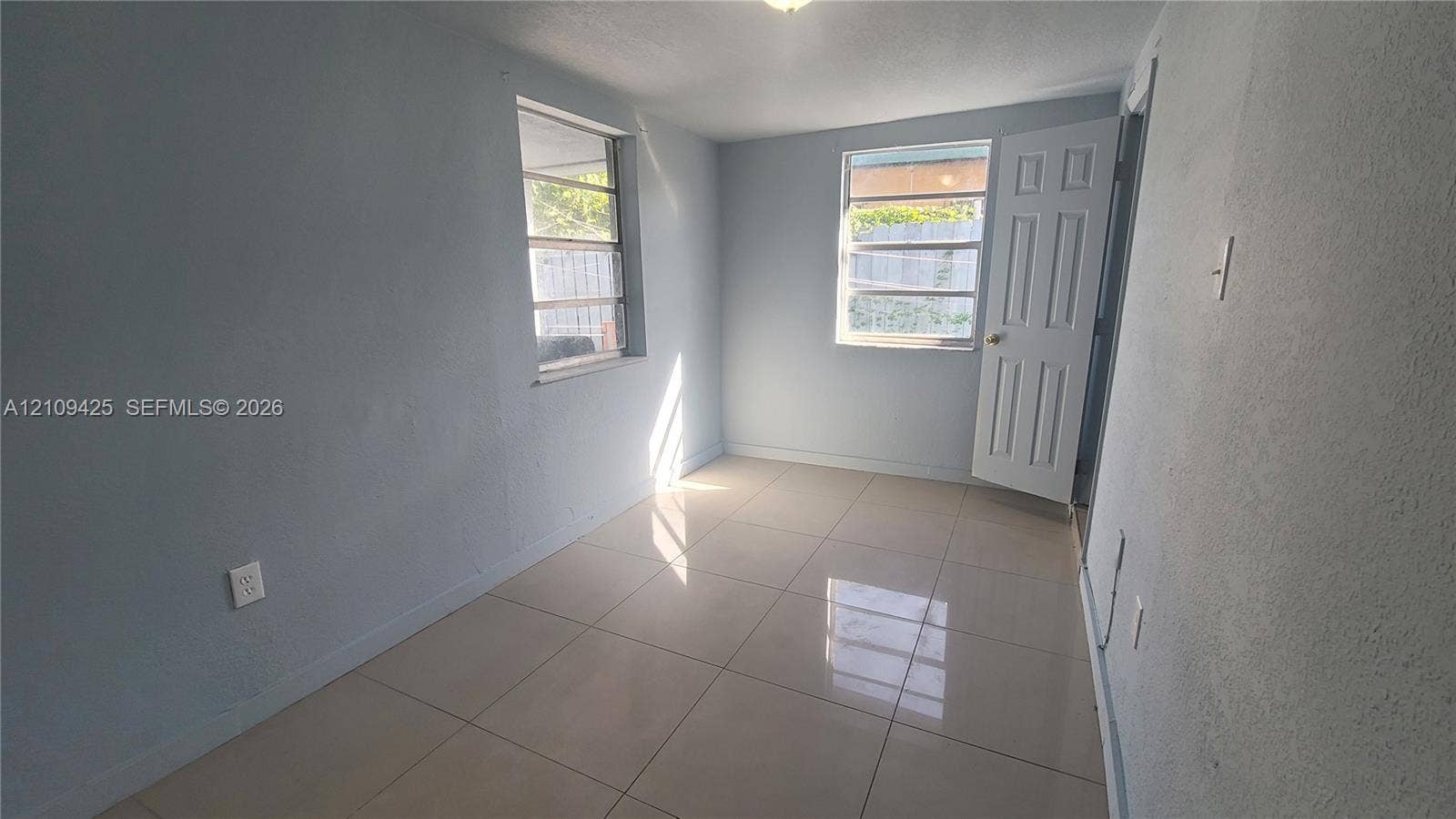 615 NW 25th Court, #B, Miami, Miami, FL 33125 Neutral-toned interior space featuring large-format tile flooring, two multi-pane windows, and a six-panel door