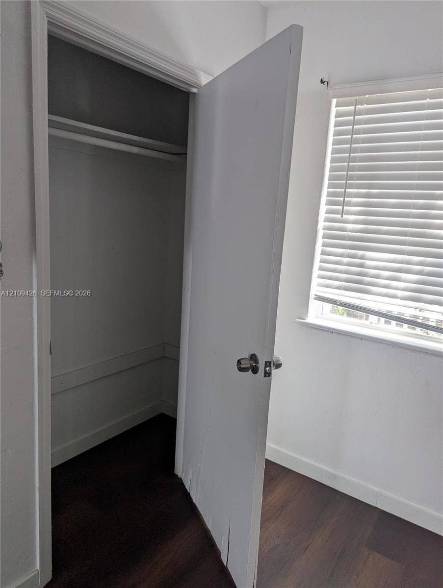 Interior space featuring wood-finish flooring, a built-in closet with an overhead shelf and clothing rod, and a window with horizontal blinds