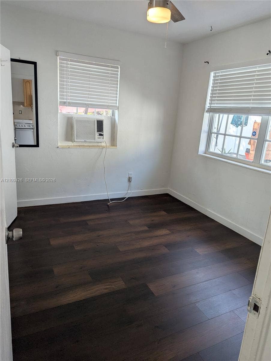 Room featuring wood-finish flooring, two windows with horizontal blinds, and a central ceiling fan with an integrated light fixture