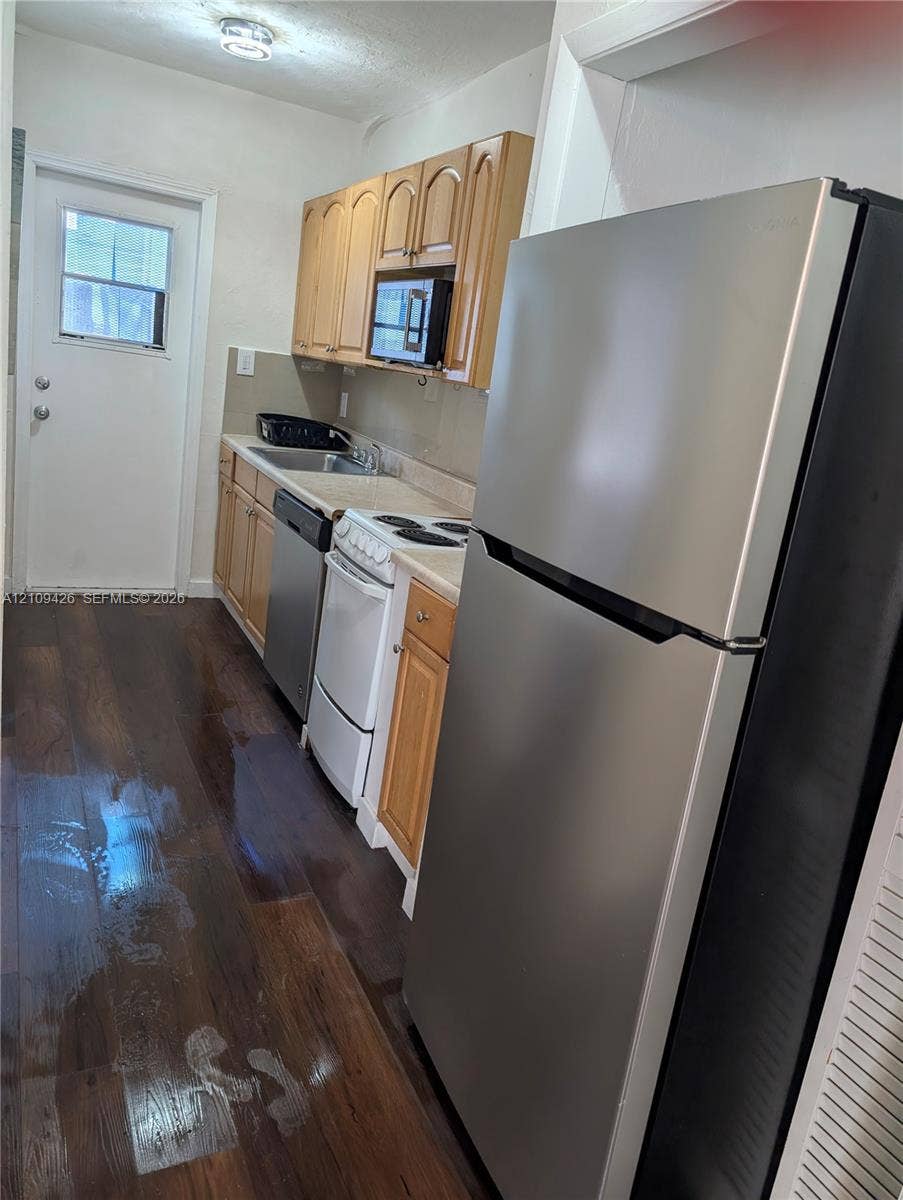 Kitchen featuring wood-finish flooring, shaker-style cabinetry, a stainless steel refrigerator, a built-in microwave, and an exterior door