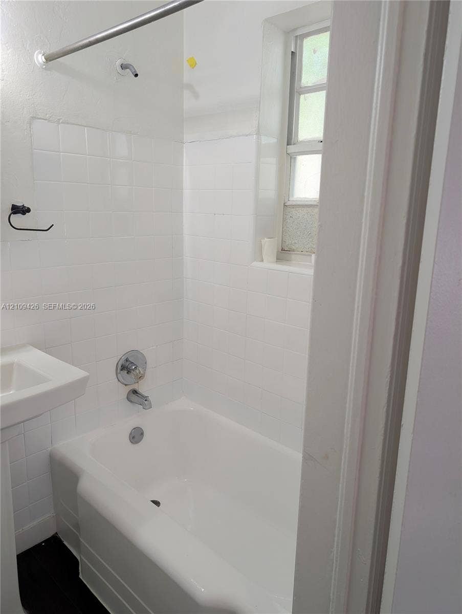 Bathroom featuring a white bathtub, white ceramic wall tile surround, pedestal sink, chrome hardware, and a vertical window