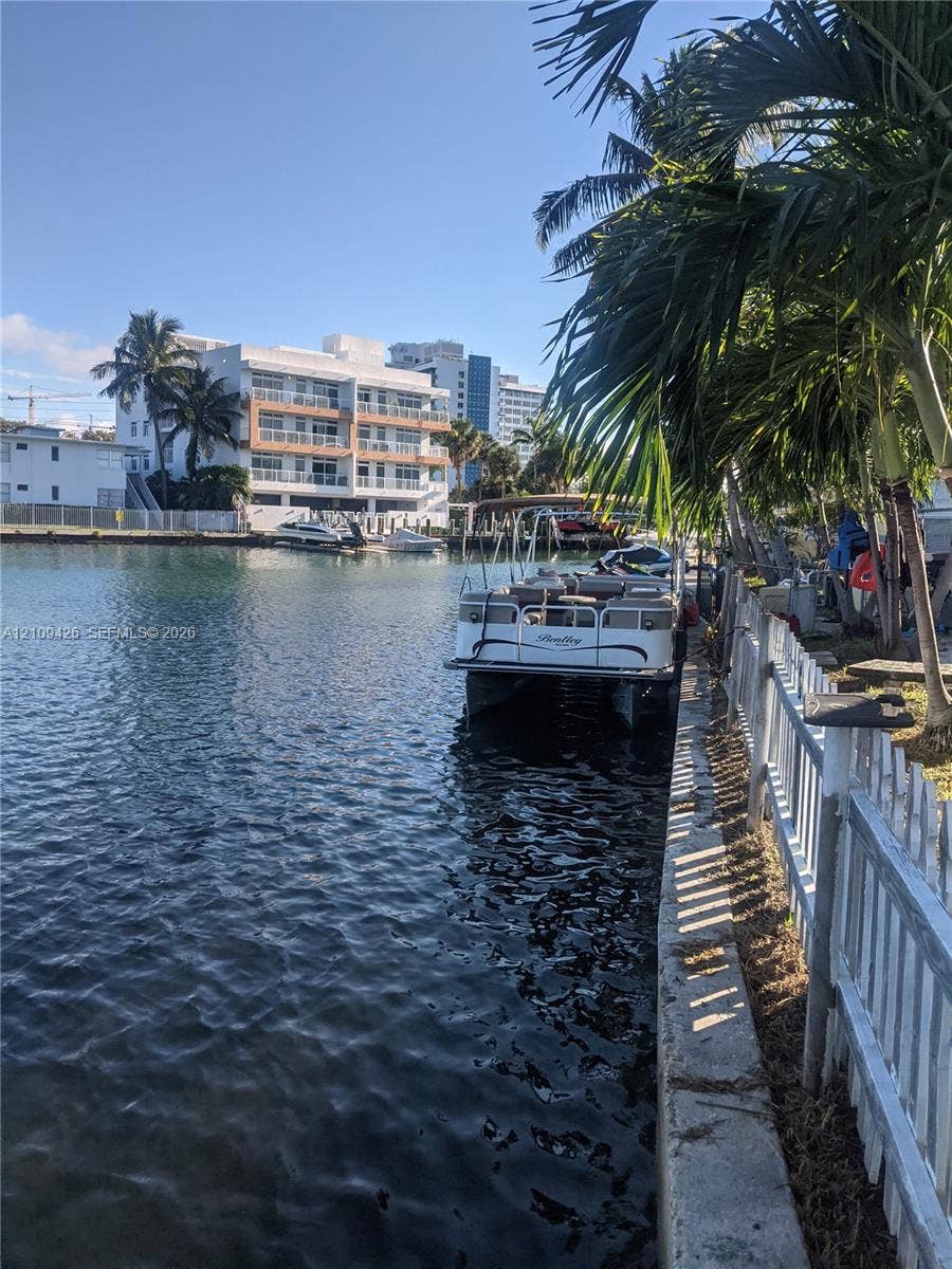 Waterfront property featuring a concrete seawall, picket fencing, and mature palm trees