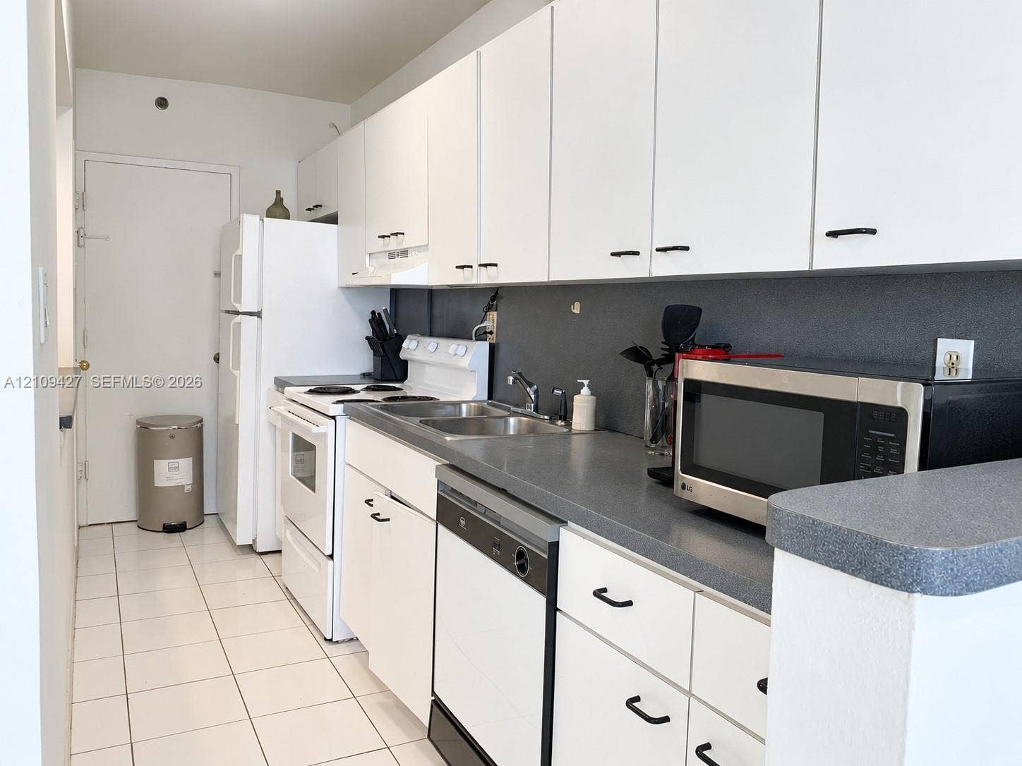Kitchen featuring white cabinetry, gray solid-surface countertops, a stainless steel double-basin sink, and white ceramic tile flooring