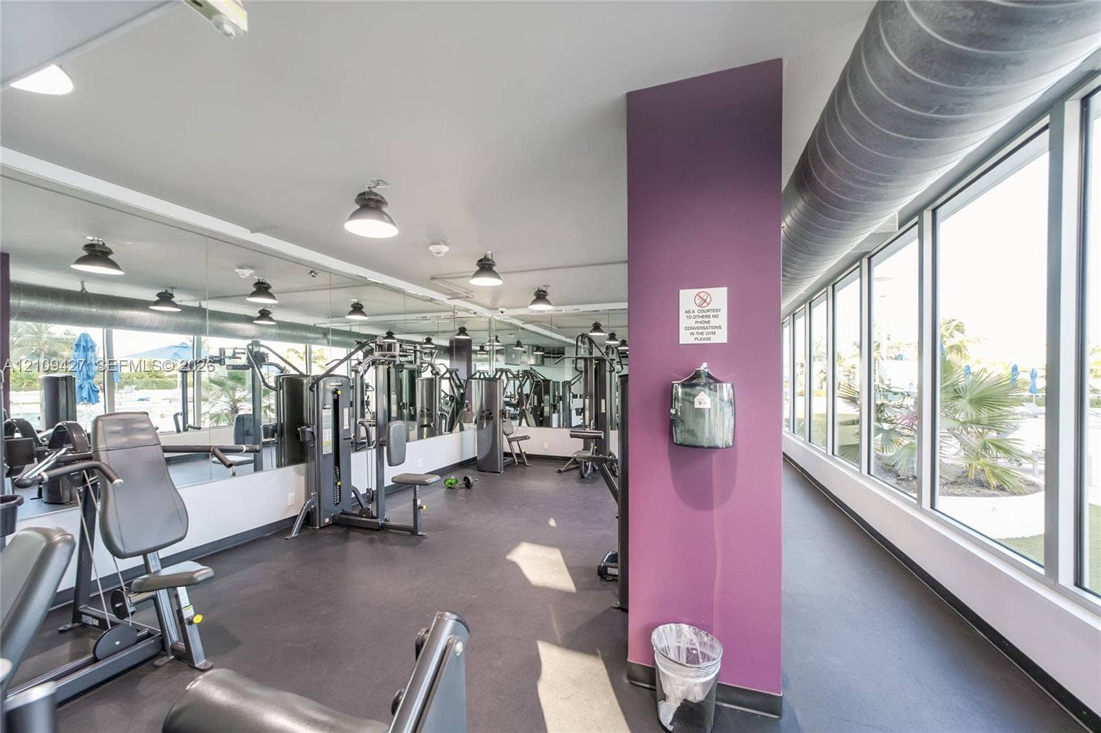 Fitness center featuring floor-to-ceiling windows, full-wall mirrors, exposed ductwork, rubberized flooring, and recessed lighting