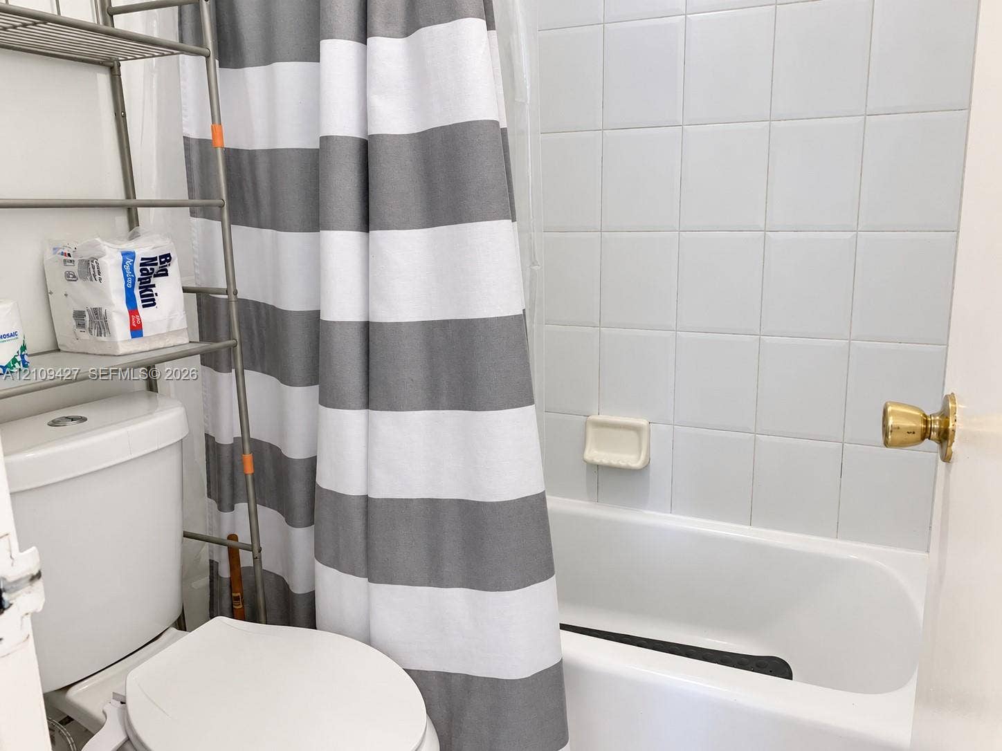 Bathroom featuring a white porcelain toilet, a bathtub with a tiled surround, and brass-tone hardware