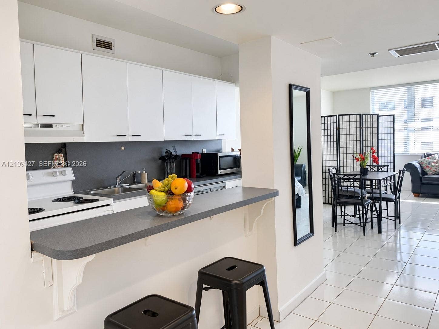 Kitchen featuring white cabinetry, gray solid-surface countertops, integrated breakfast bar, and white tile flooring