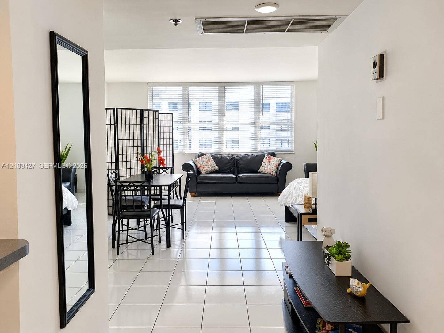 Bright, open-concept interior featuring white ceramic tile flooring and floor-to-ceiling windows with horizontal blinds