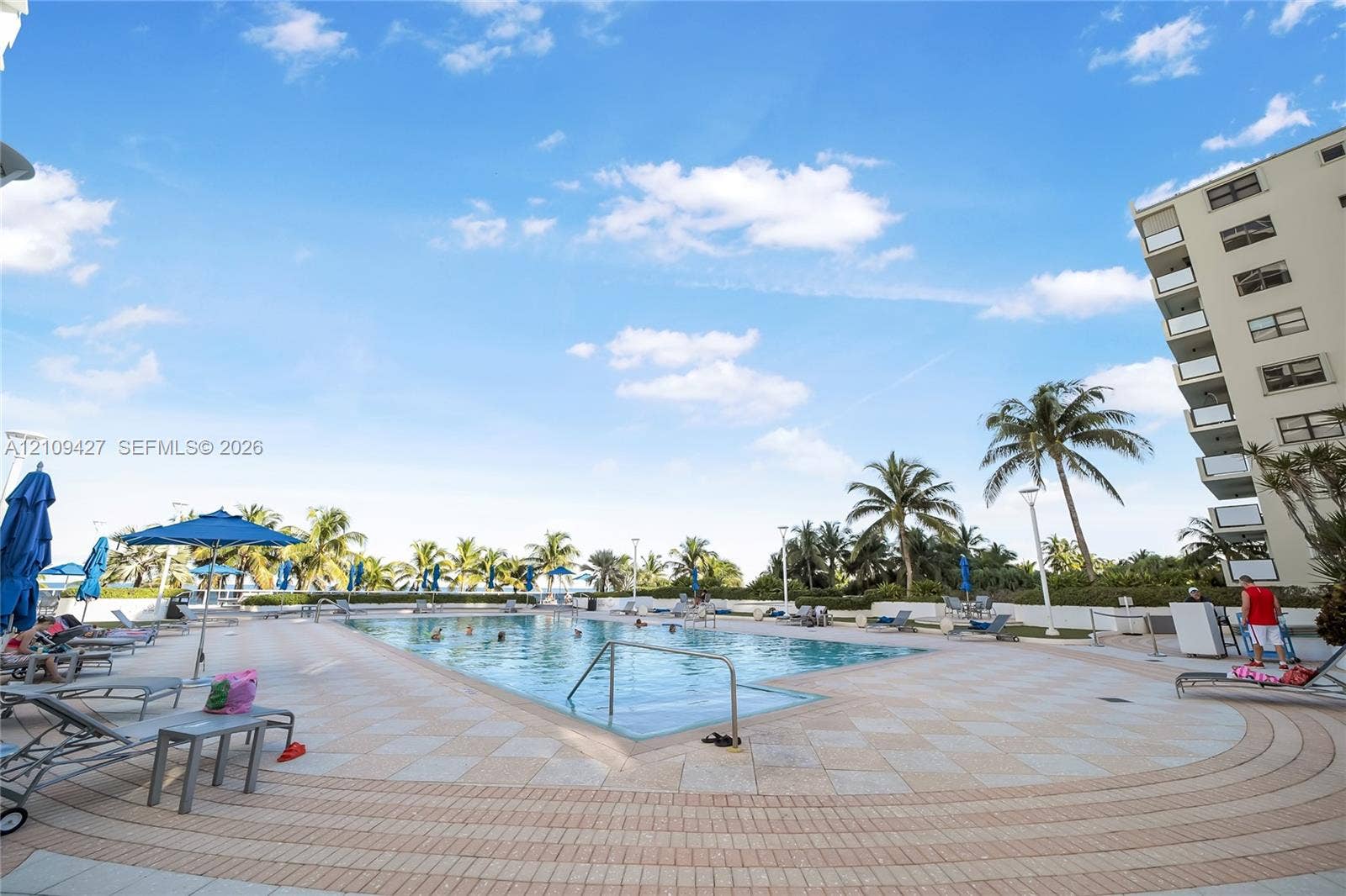 Outdoor swimming pool surrounded by a paved deck, perimeter palm trees, and structural balcony access