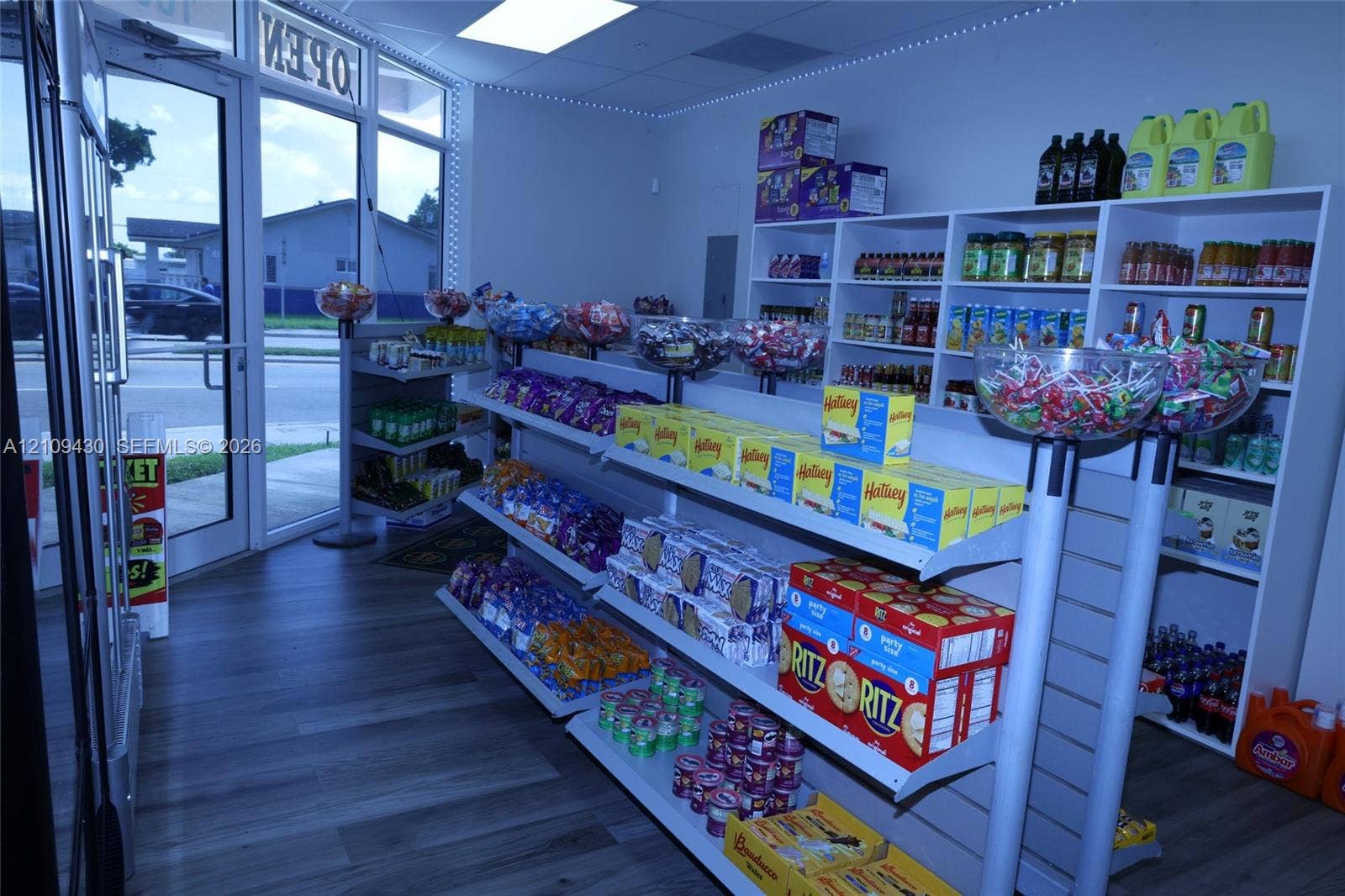 Commercial interior featuring wood-finish flooring, floor-to-ceiling glass-paneled entry door, built-in slat-wall shelving, and recessed ceiling lighting