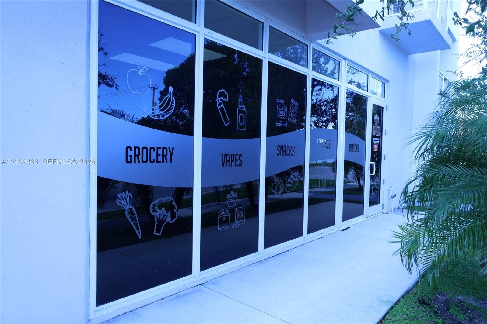 Commercial storefront featuring a white stucco exterior, expansive floor-to-ceiling glass windows, and a dedicated concrete pedestrian walkway