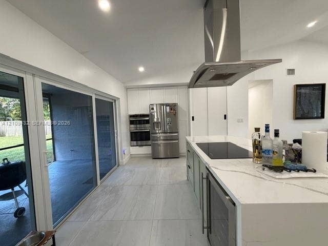 254 NW 107th Terrace, Coral Springs, FL 33071 Kitchen featuring a large waterfall-edge island with an integrated cooktop and under-counter refrigeration, stainless steel wall-mounted range hood, custom cabinetry, stainless steel double wall ovens, and expansive sliding glass doors