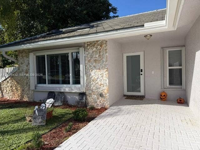 254 NW 107th Terrace, Coral Springs, FL 33071 Exterior featuring stone veneer accents, a covered entryway with light-toned herringbone paver flooring, a bay window with multi-pane framing, and a glass-paneled entry door