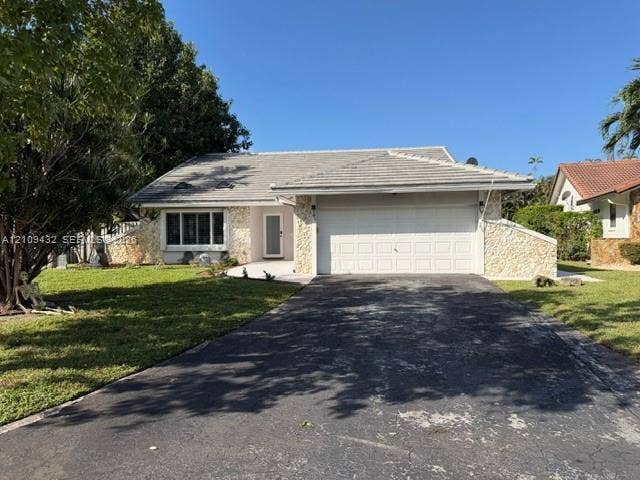 254 NW 107th Terrace, Coral Springs, FL 33071 Single-story residence featuring a stone veneer facade, concrete tile roof, two-car garage, and a paved driveway