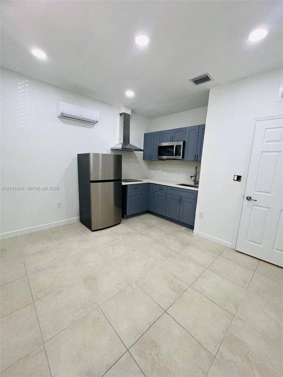 24161 SW 115th Court, #1, Homestead, Homestead, FL 33032 Kitchen featuring blue shaker-style cabinetry, stainless steel appliances, a chimney-style range hood, solid-surface countertops, and light-tone tile flooring