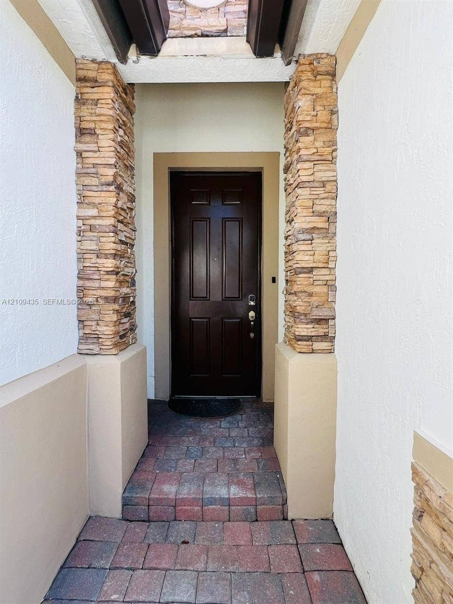 24161 SW 115th Court, #1, Homestead, Homestead, FL 33032 Covered entryway featuring stone veneer columns, a multi-paneled dark wood-finish door, and paver stone flooring