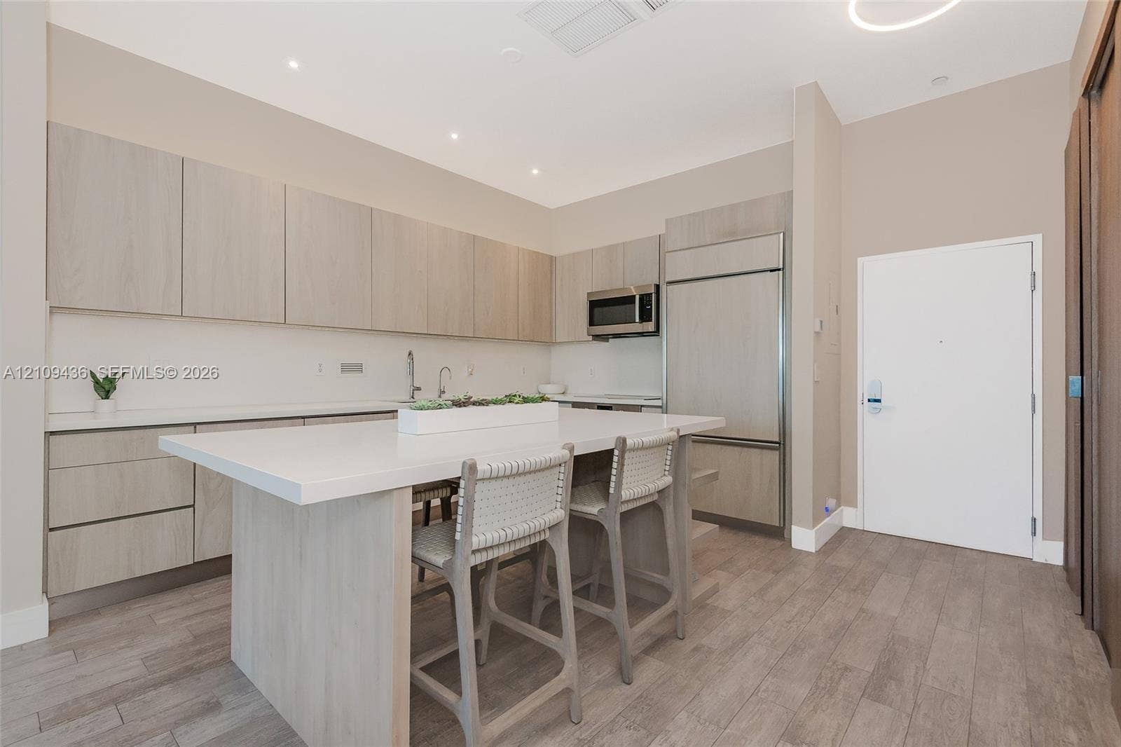 Kitchen featuring wood-finish cabinetry, stone-surface center island, stainless steel built-in appliances, and wood-finish flooring