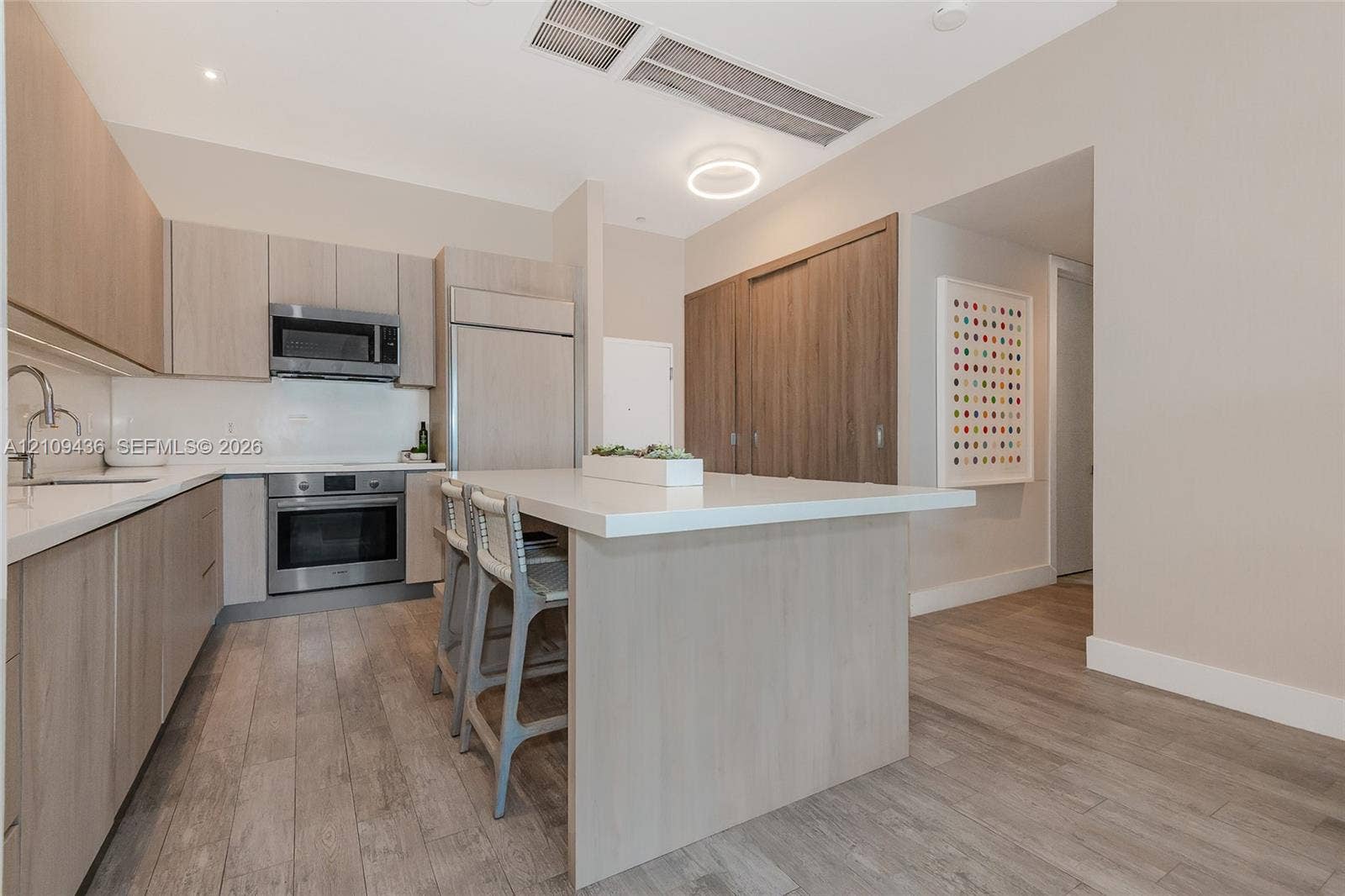 Kitchen featuring light wood-finish cabinetry, quartz countertops, a central island, stainless steel appliances, and wood-finish flooring