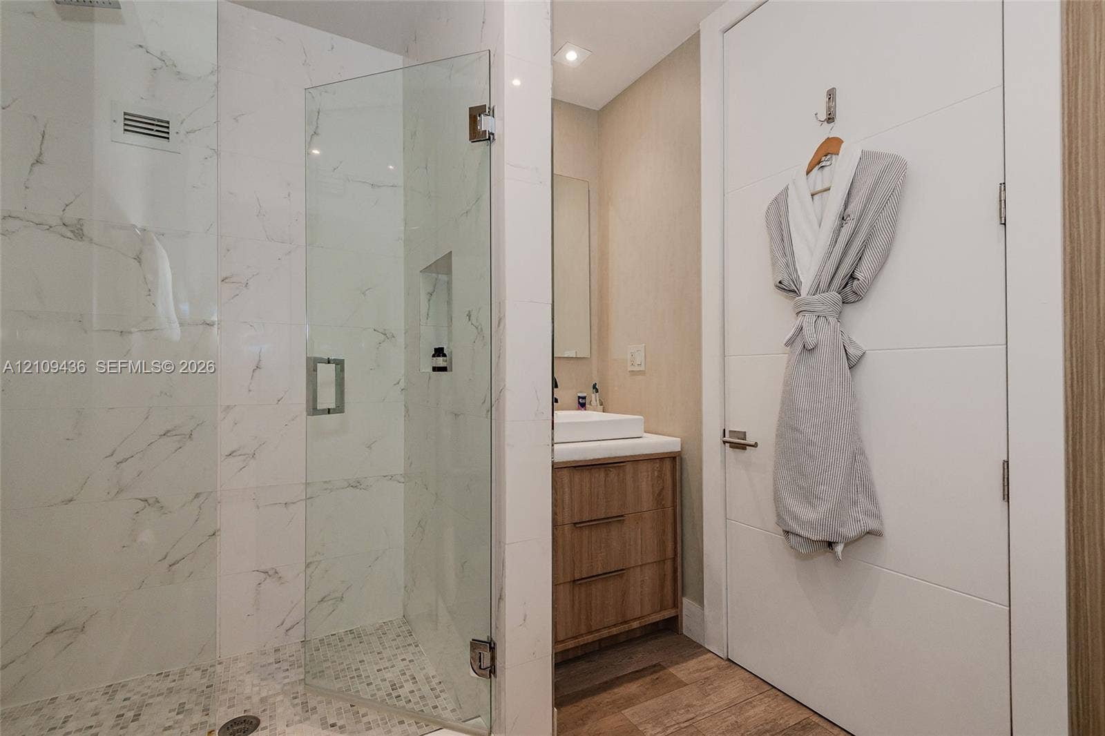 Walk-in shower featuring glass paneling, marble-style tile walls, and a pebble-stone floor, paired with a wood-finish vanity, vessel sink, and solid-core door