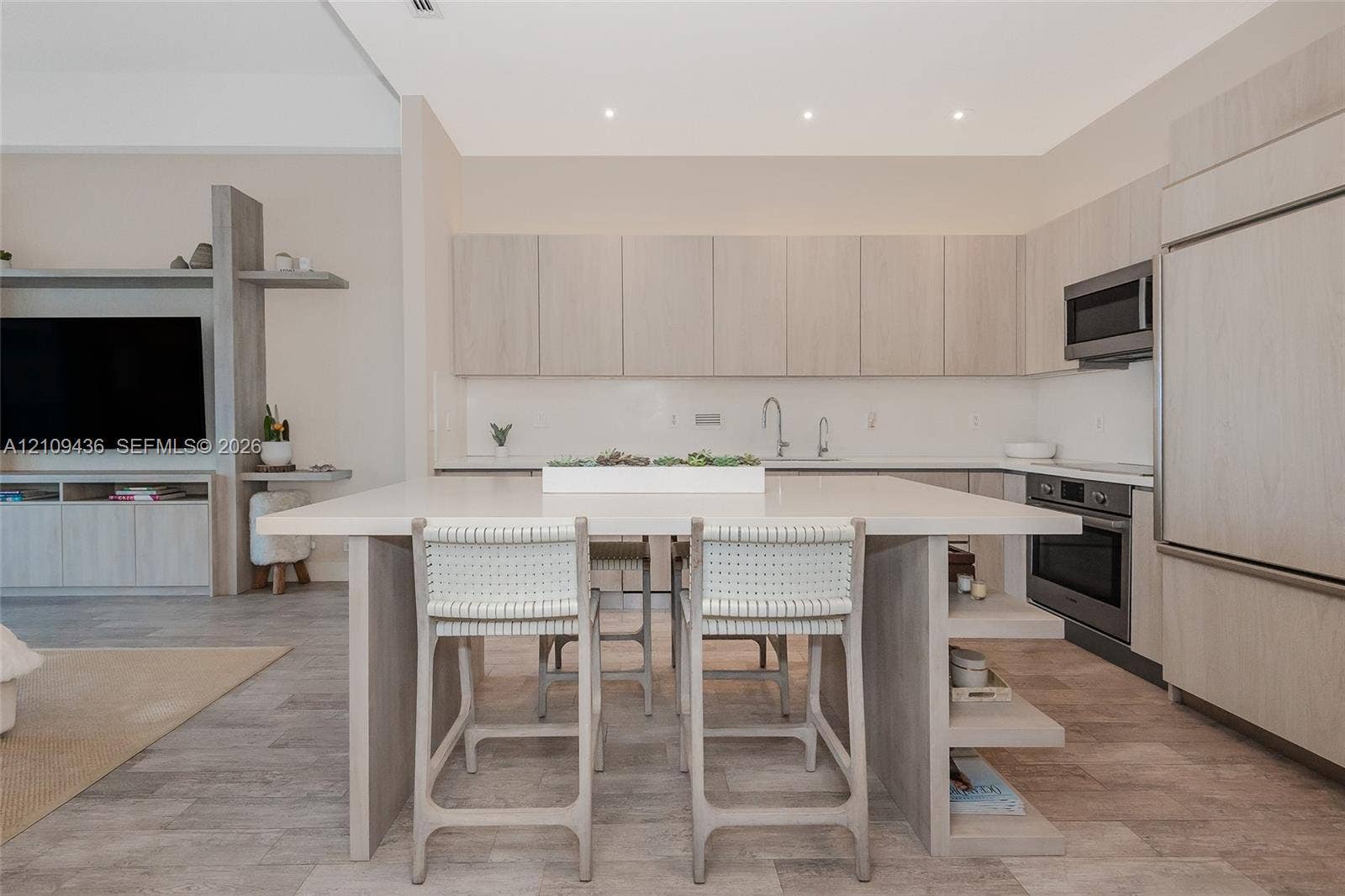Modern kitchen featuring light wood-finish cabinetry, a large central island with a solid surface countertop, integrated stainless steel appliances, recessed lighting, and wood-finish tile flooring