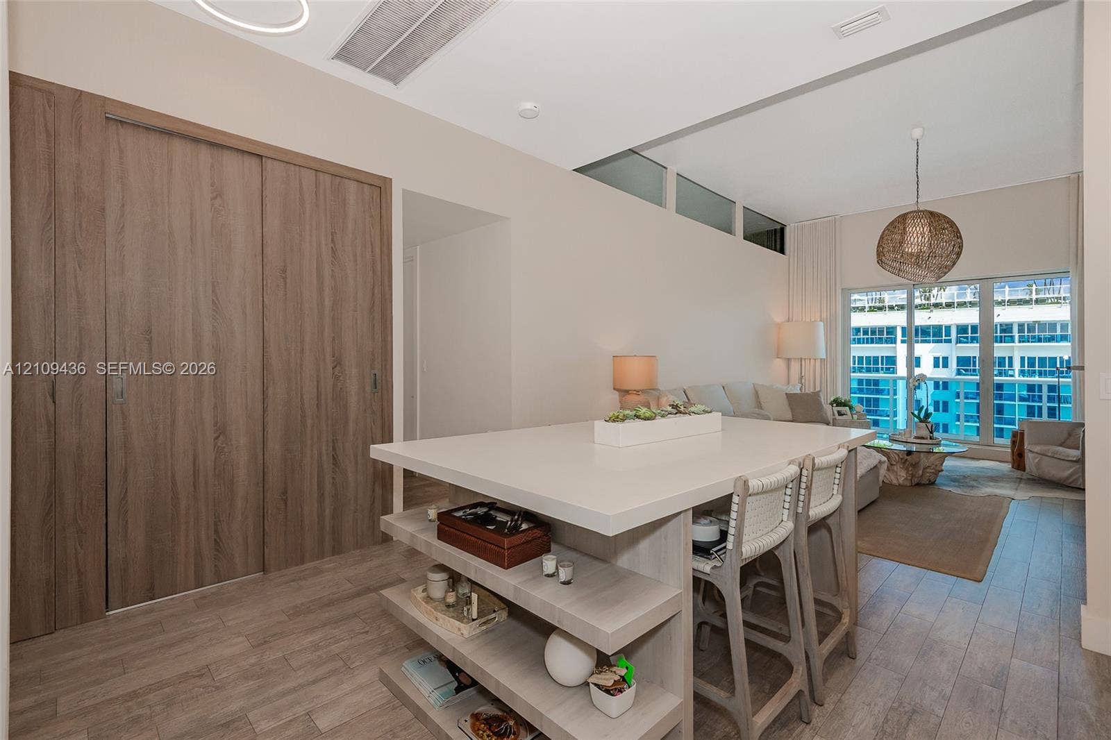 Central island with integrated shelving and solid surface countertop, wood-finish flooring, floor-to-ceiling wood-finish sliding doors, and clerestory windows