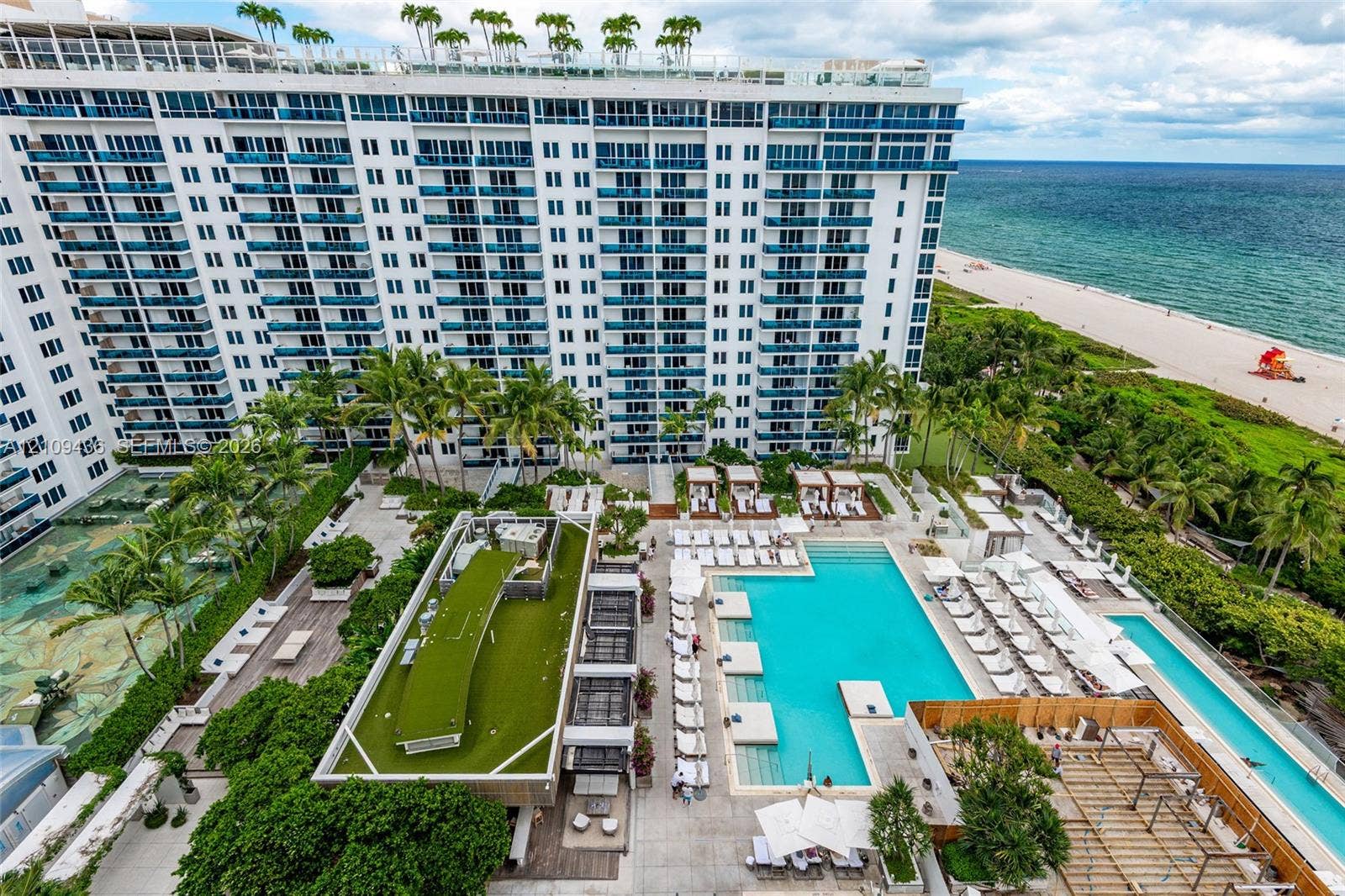 Multi-story beachfront high-rise featuring expansive exterior balconies, resort-style swimming pools, landscaped sundecks, and direct proximity to the oceanfront