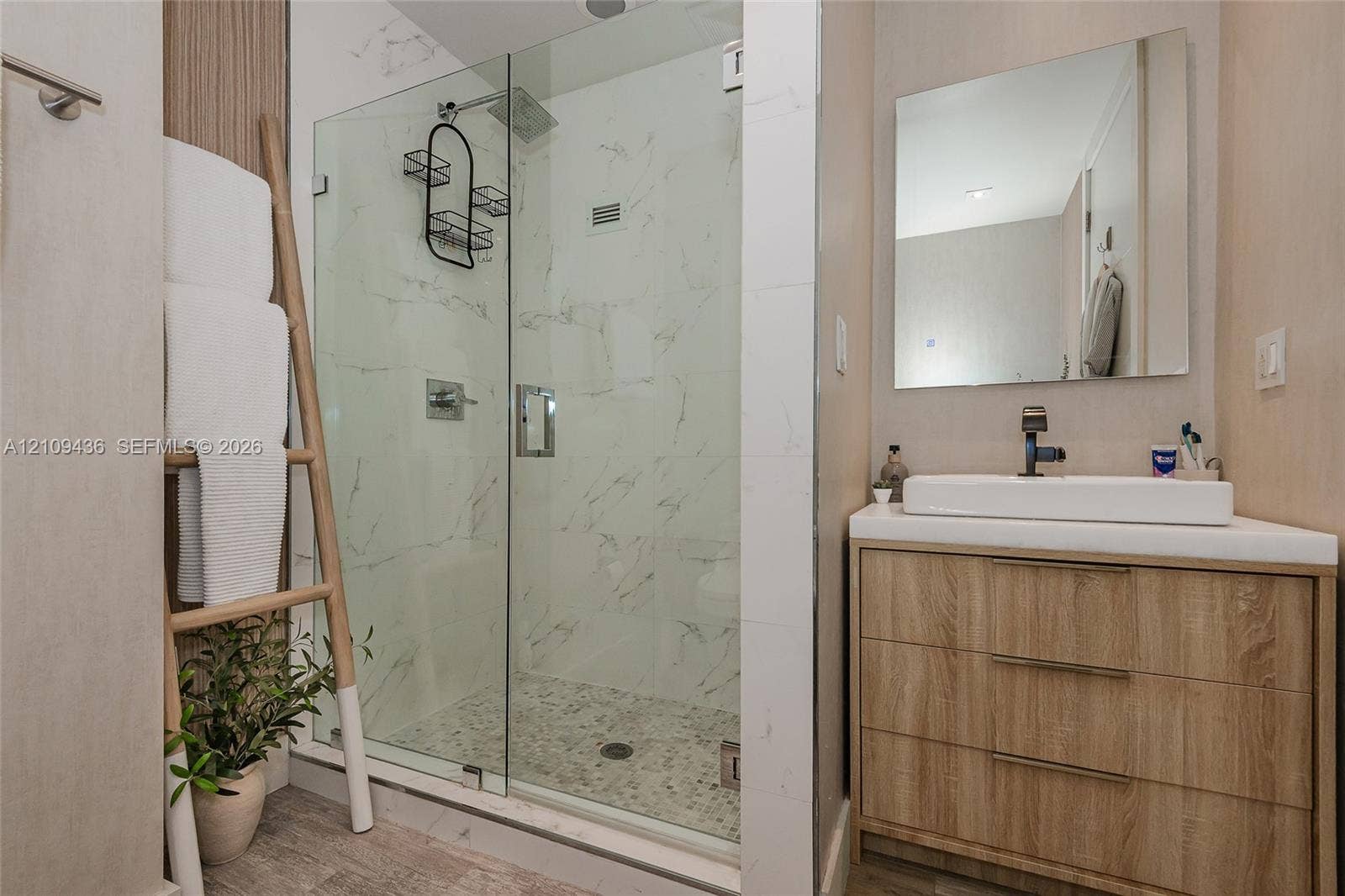 Walk-in shower with stone-finish wall tile, pebble-style flooring, and frameless glass door