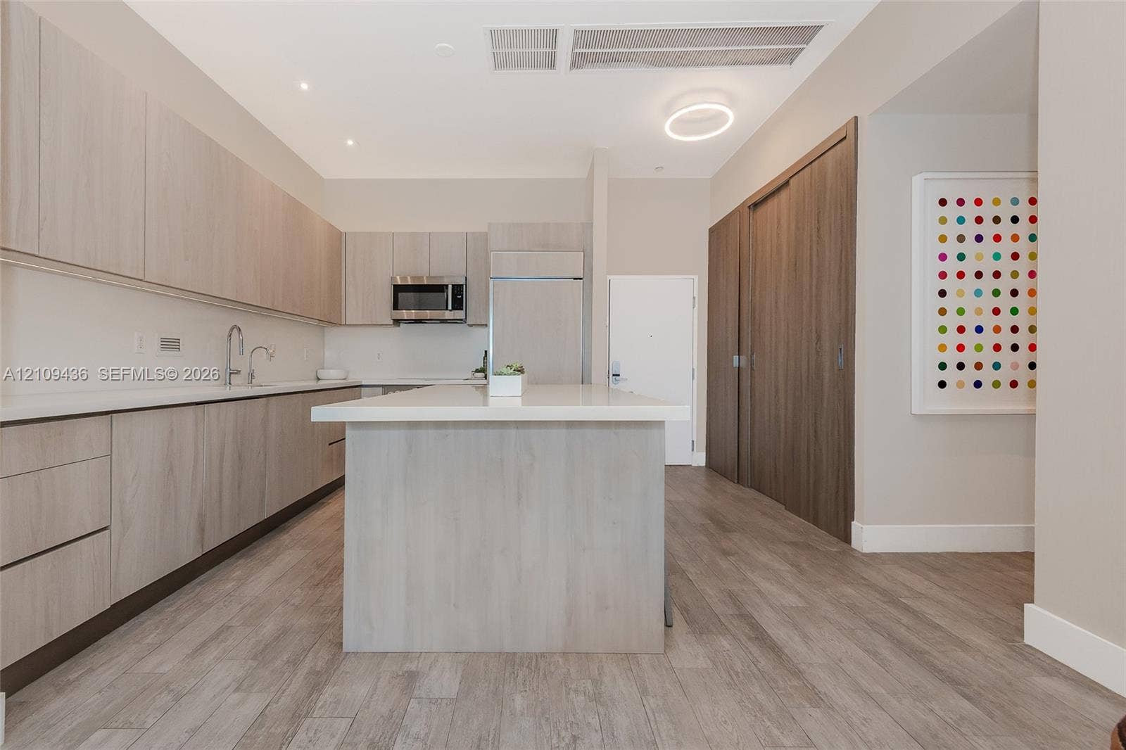 Kitchen featuring wood-finish cabinetry, stone-surface countertops, an integrated island, stainless steel appliances, and wood-finish flooring