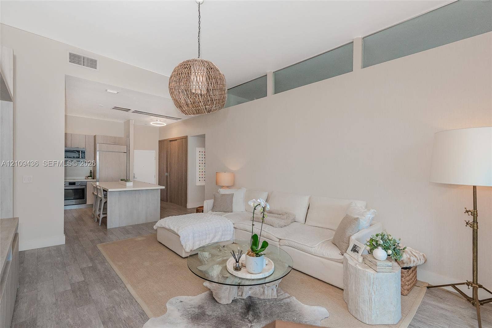 High-ceiling living area featuring clerestory windows, wood-finish flooring, a woven pendant light fixture, and an integrated kitchen with a stone-surface island