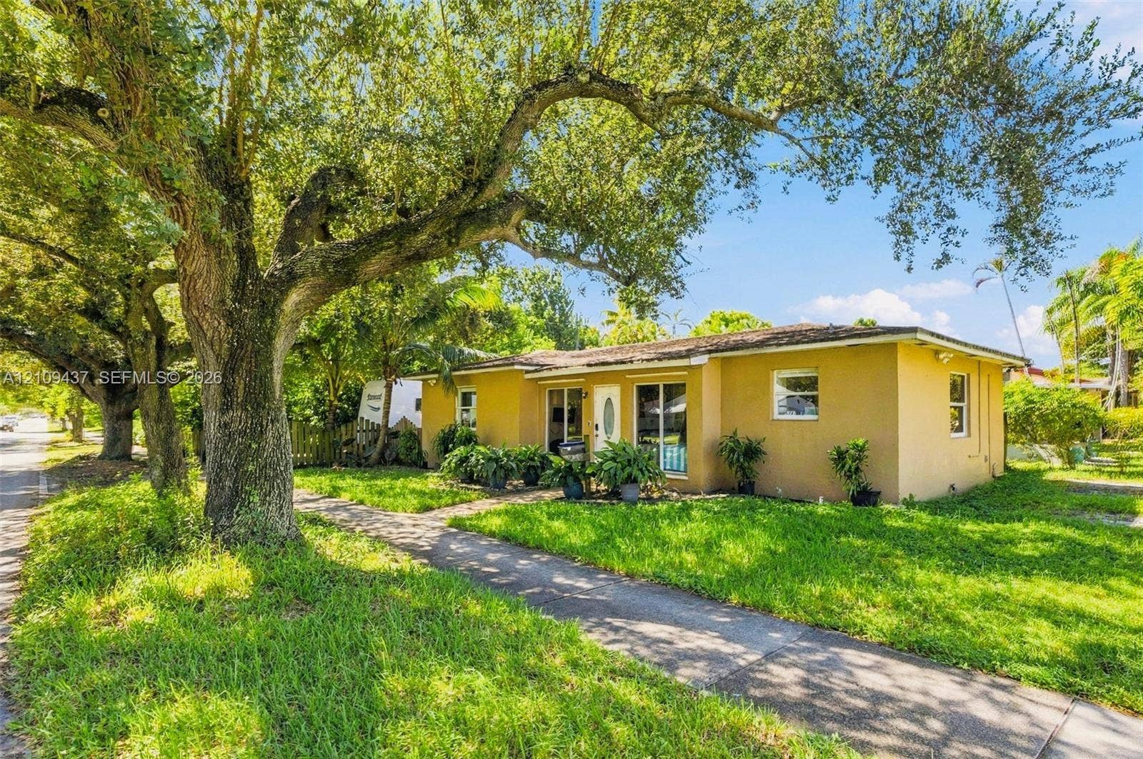 Stucco exterior residence featuring mature oak trees, a concrete walkway, and expansive green space