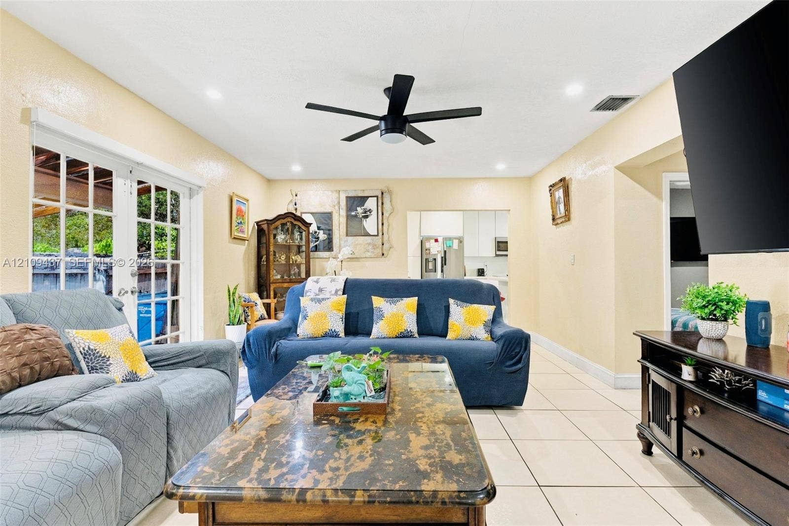 Living area featuring large format neutral tile flooring, recessed lighting, a modern matte black ceiling fan, and multi-panel glass French doors