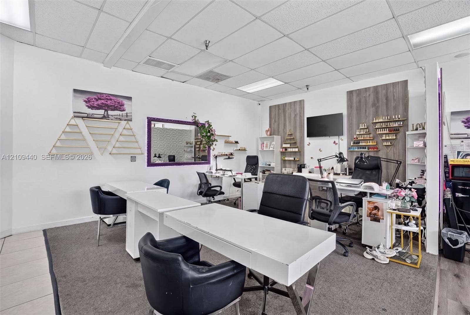 Commercial workspace featuring a suspended acoustic tile ceiling, recessed lighting, wall-mounted display shelving, wood-finish wall paneling, and mirrored wall accents