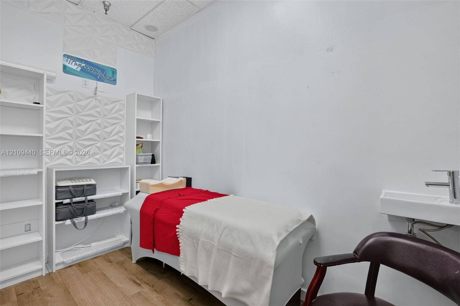 Room featuring wood-finish flooring, built-in shelving, decorative textured wall panels, and a wall-mounted sink with a chrome faucet