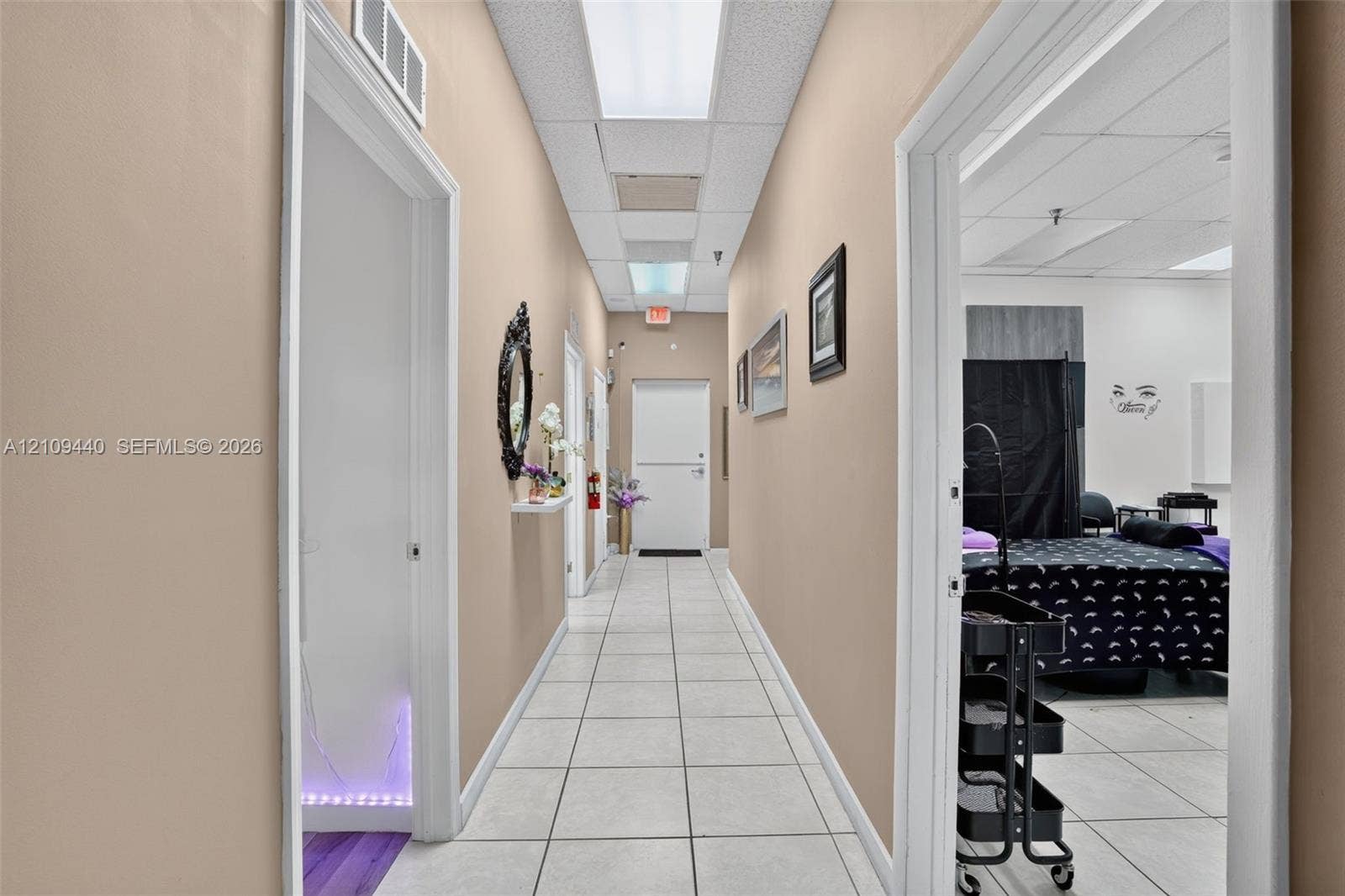 Interior hallway featuring white tile flooring, recessed drop-ceiling lighting, and multiple entryways with clean white trim