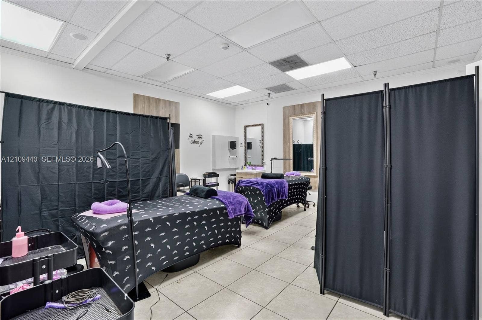 Commercial space featuring neutral tile flooring, recessed drop-ceiling lighting, and wall-mounted vanity mirrors with wood-finish trim