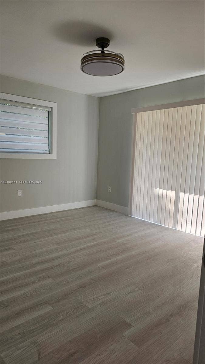 Neutral wall tones, wood-finish flooring, ceiling-mounted light fixture, sliding glass door with vertical blinds, and window with horizontal blinds