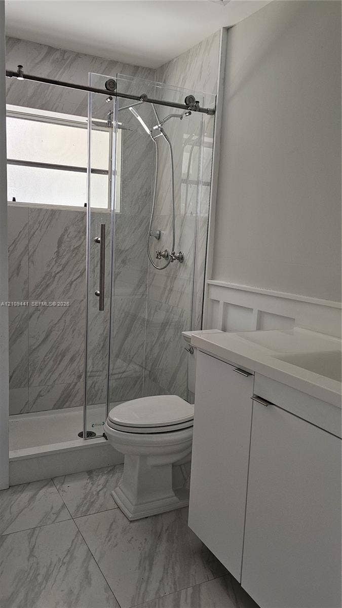 Walk-in shower with sliding glass door, stone-finish wall tile, white vanity with integrated sink, and wainscoting detail