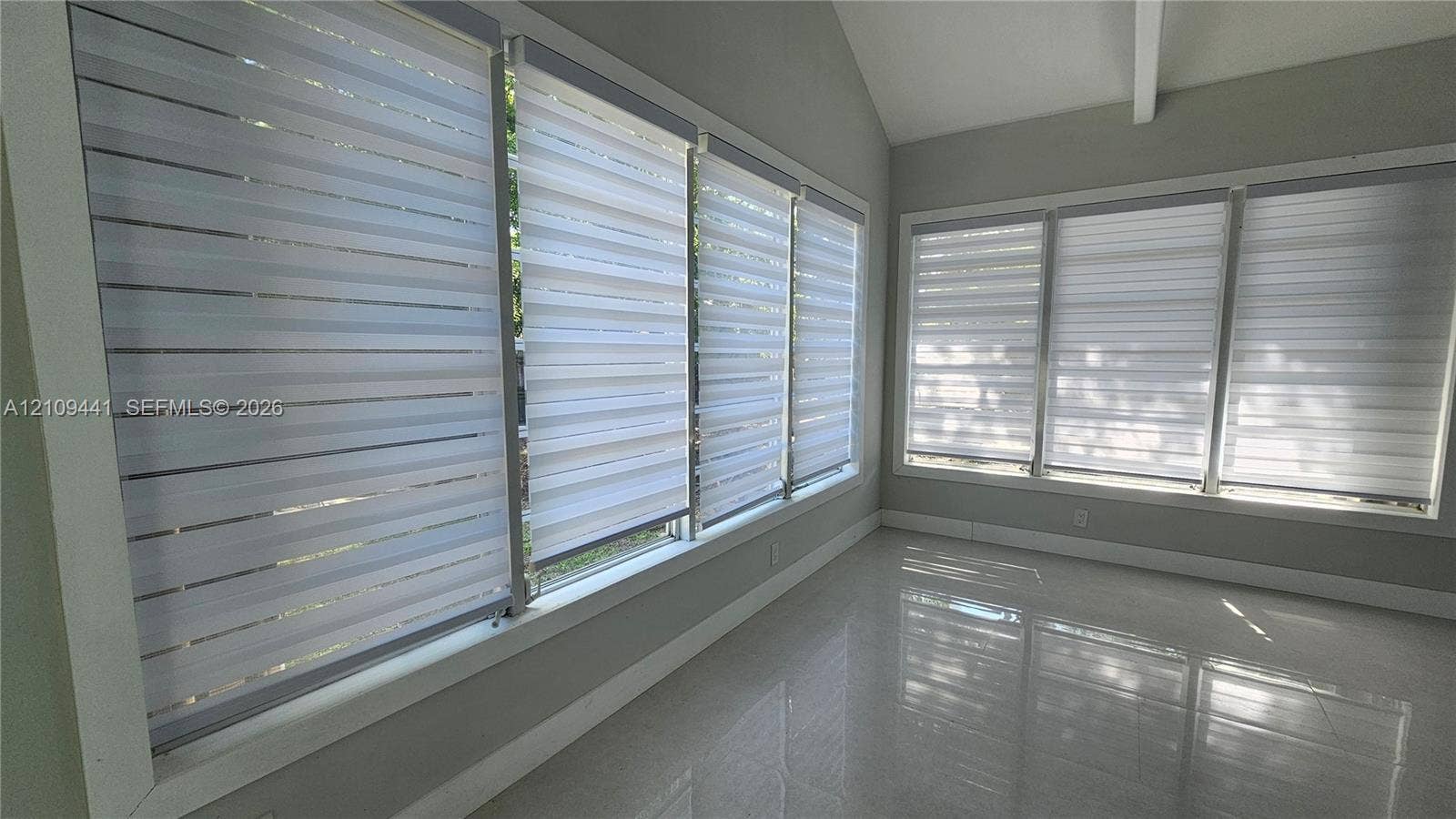 Vaulted ceiling featuring a central support beam, large windows with horizontal roller shades, and polished tile flooring