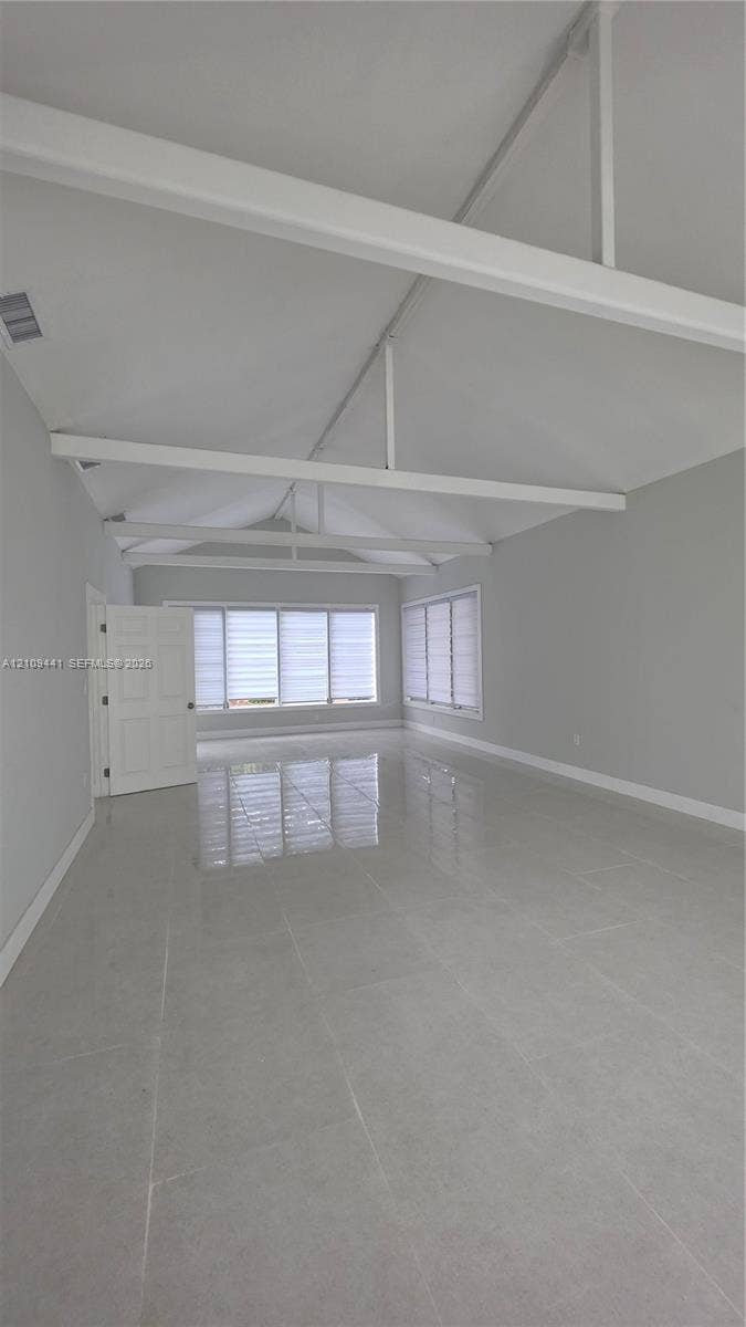 Vaulted ceiling with exposed white beams, large-format tile flooring, and multiple windows with horizontal blinds