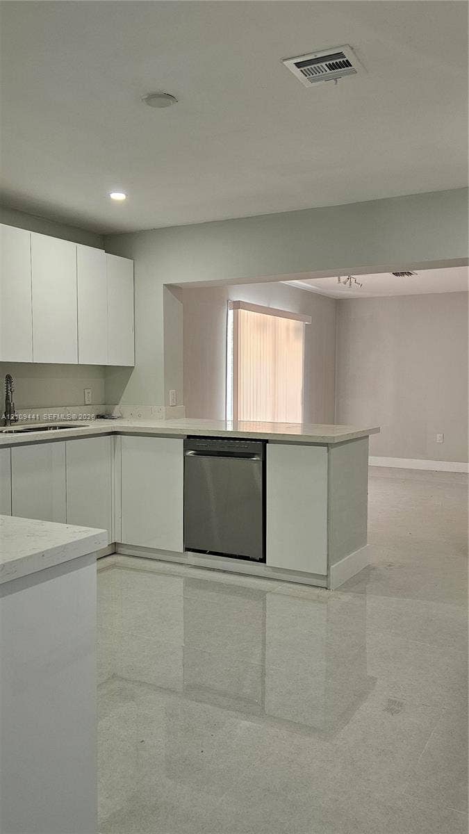 Kitchen featuring white flat-panel cabinetry, stone-style countertops, integrated stainless steel dishwasher, and polished light-toned flooring