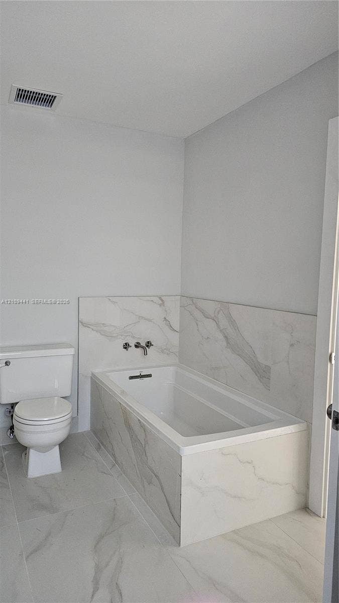 Bathroom featuring a deep soaking tub with a wall-mounted faucet, complemented by large-format tile flooring and matching tile surround