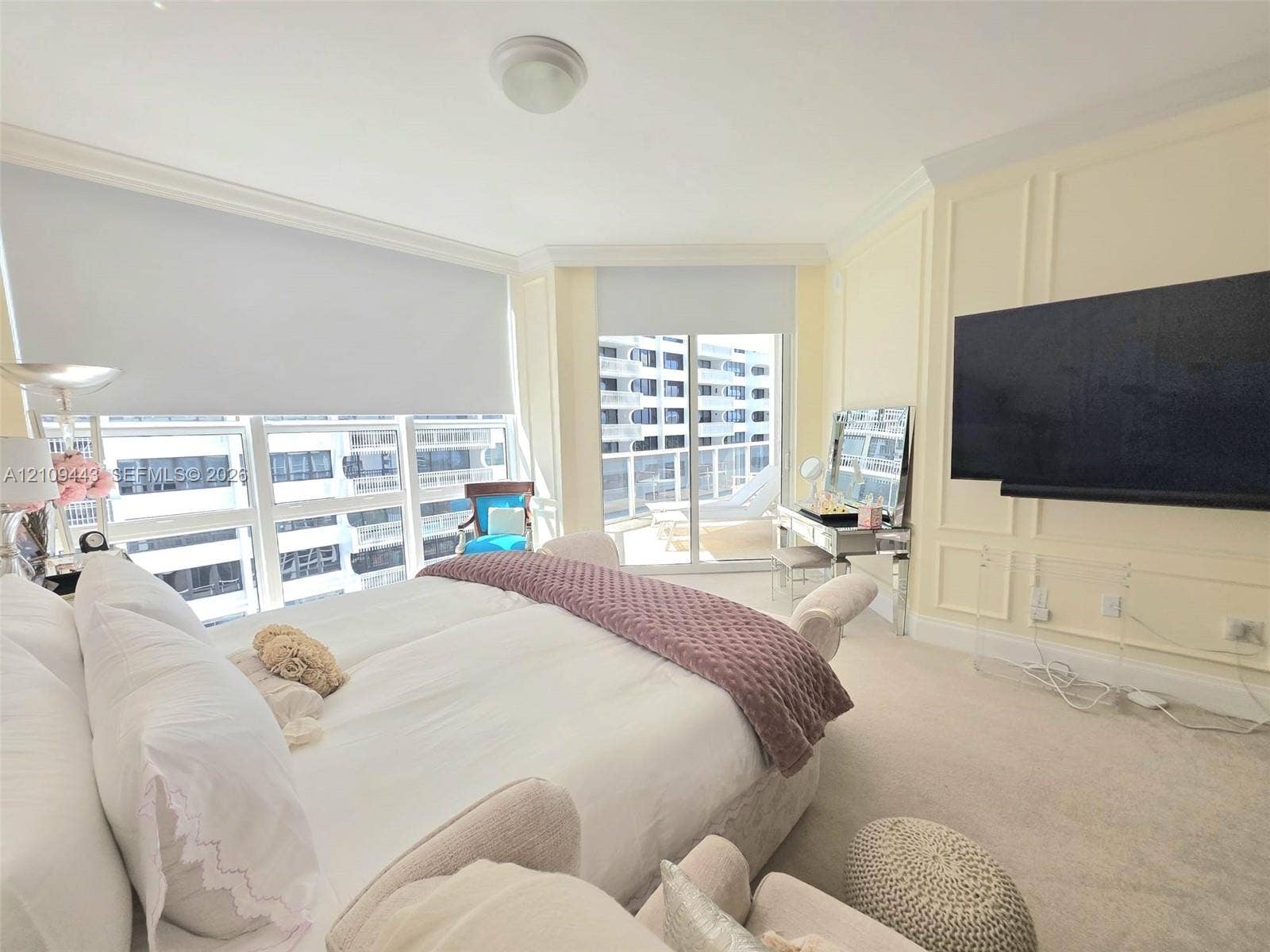 Expansive floor-to-ceiling windows, sliding glass door access to a private balcony, custom wall molding, neutral carpeting, and a ceiling-mounted light fixture
