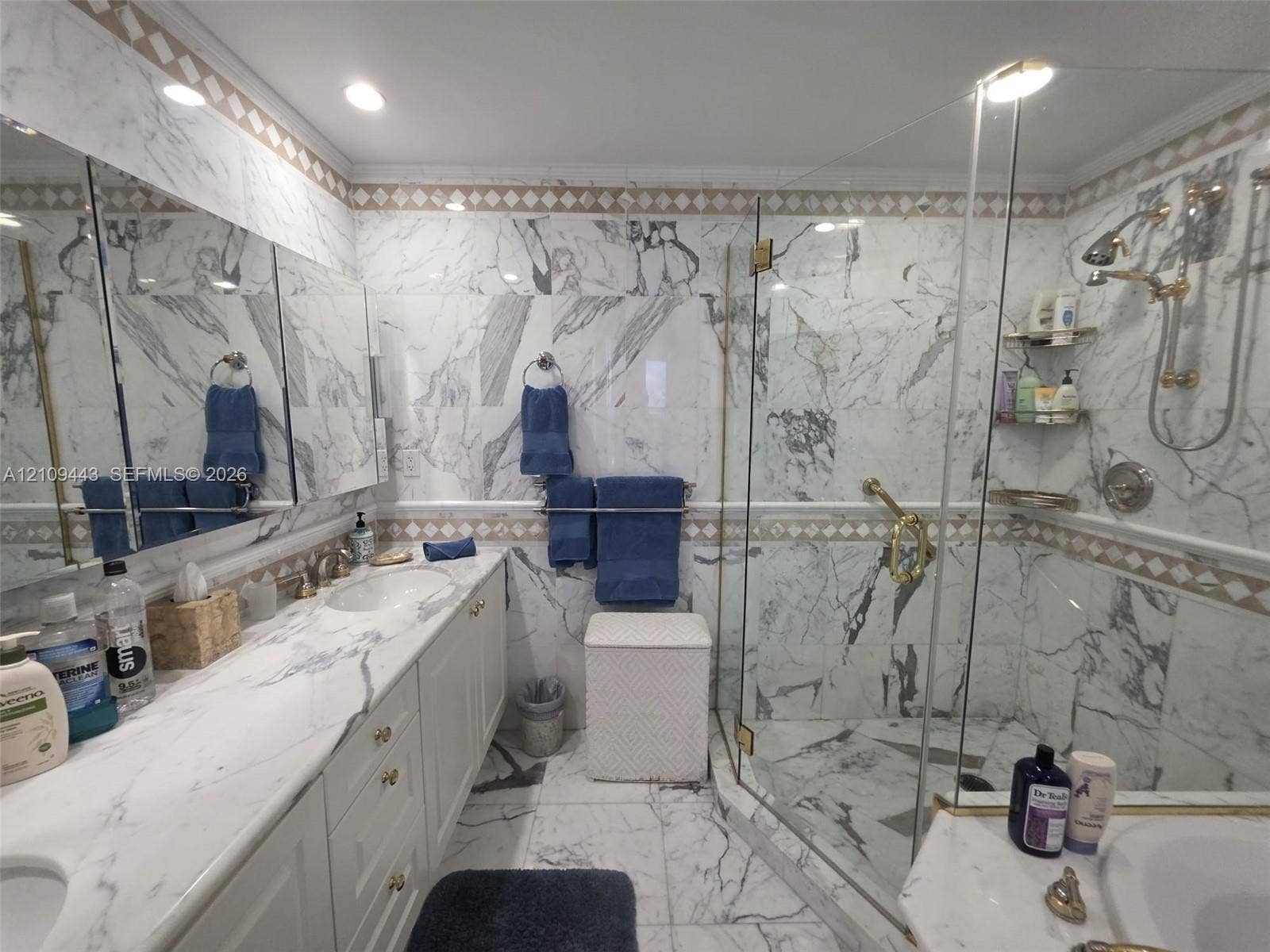 Bathroom featuring full-height stone wall tiling, a double vanity with stone countertop, recessed lighting, and a walk-in glass-enclosed shower with gold-tone hardware