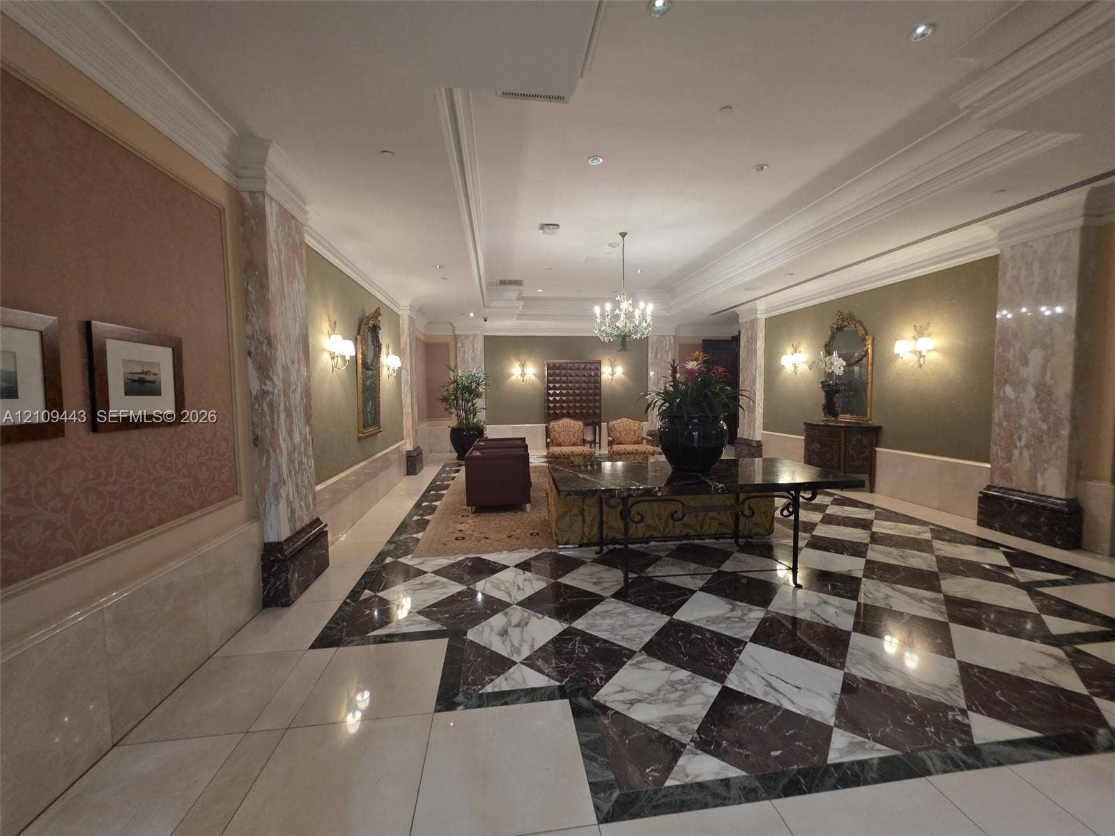 Grand entrance hall featuring patterned stone flooring, decorative stone-clad columns, recessed ceiling lighting, wall-mounted sconces, and crown molding