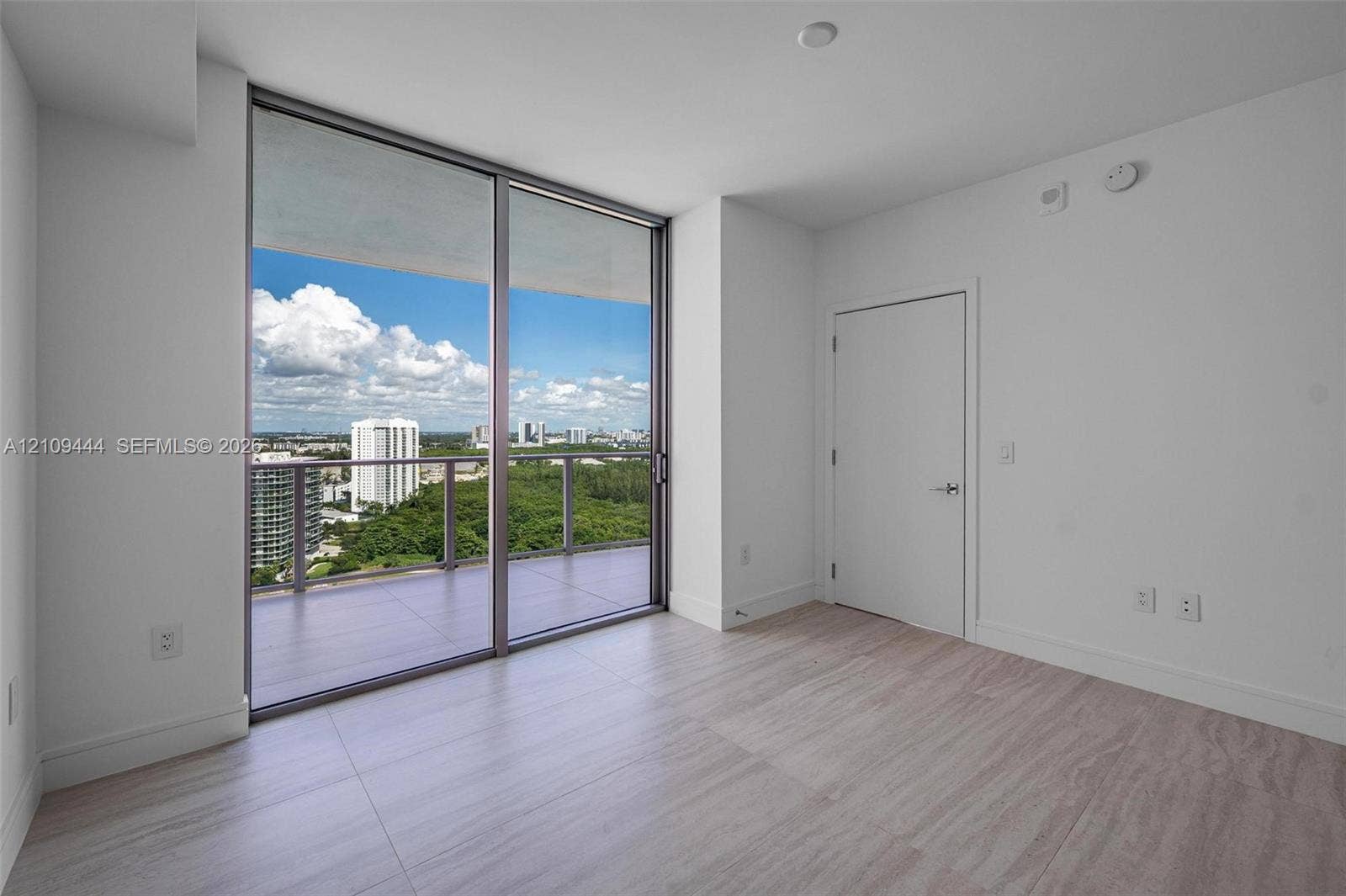 Floor-to-ceiling glass sliding doors, private balcony, wood-finish flooring, and neutral wall palette