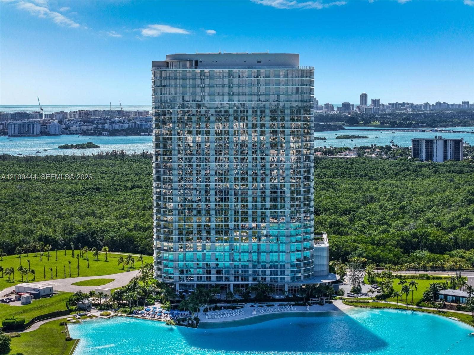 High-rise residential tower featuring a glass-curtain wall exterior, private balconies, and a multi-level structure positioned on a waterfront site with expansive green space