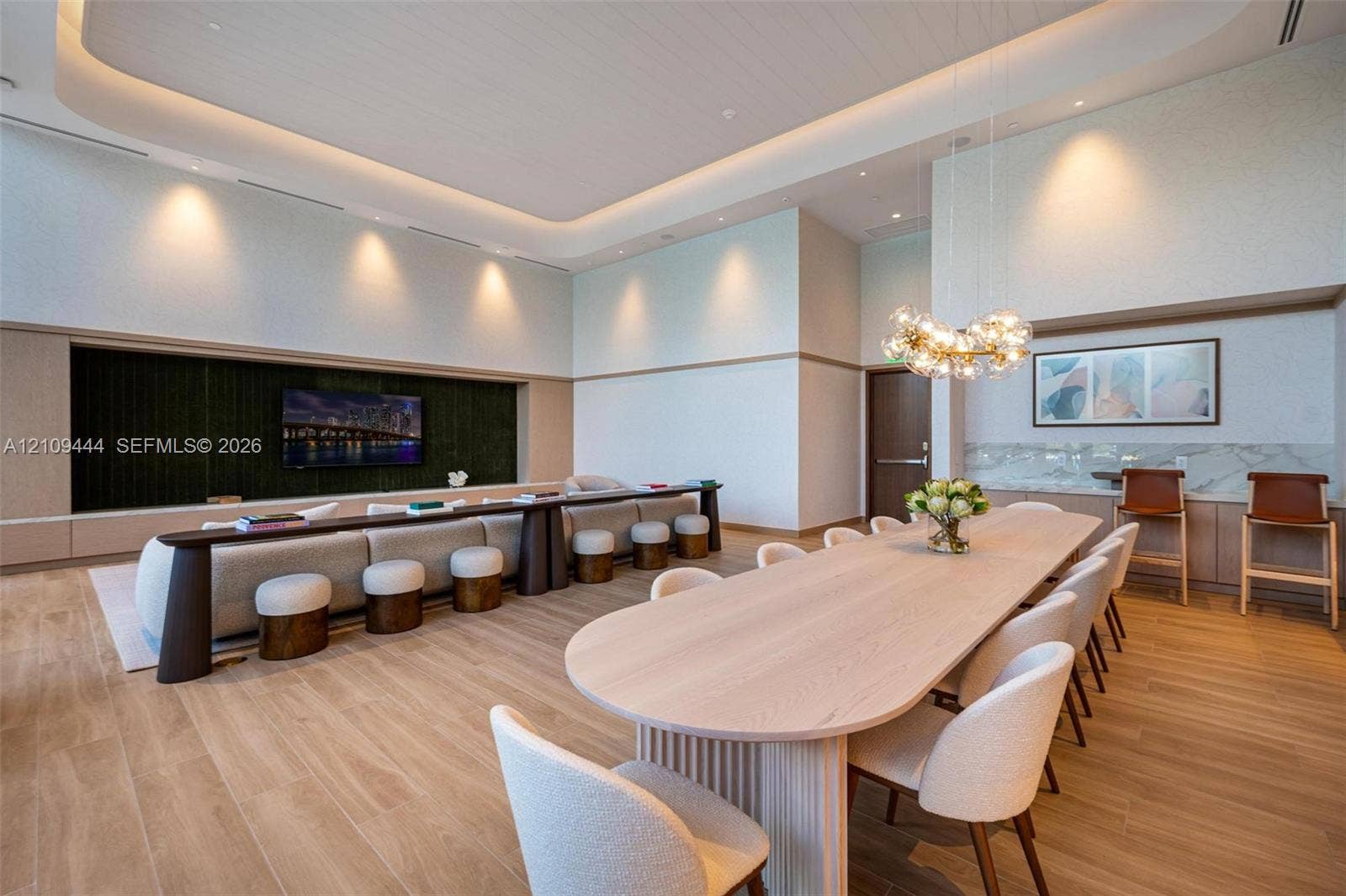 High-ceiling interior featuring recessed tray lighting, wood-finish flooring, a built-in entertainment niche, and a custom bar area with stone-finish surfacing and integrated lighting